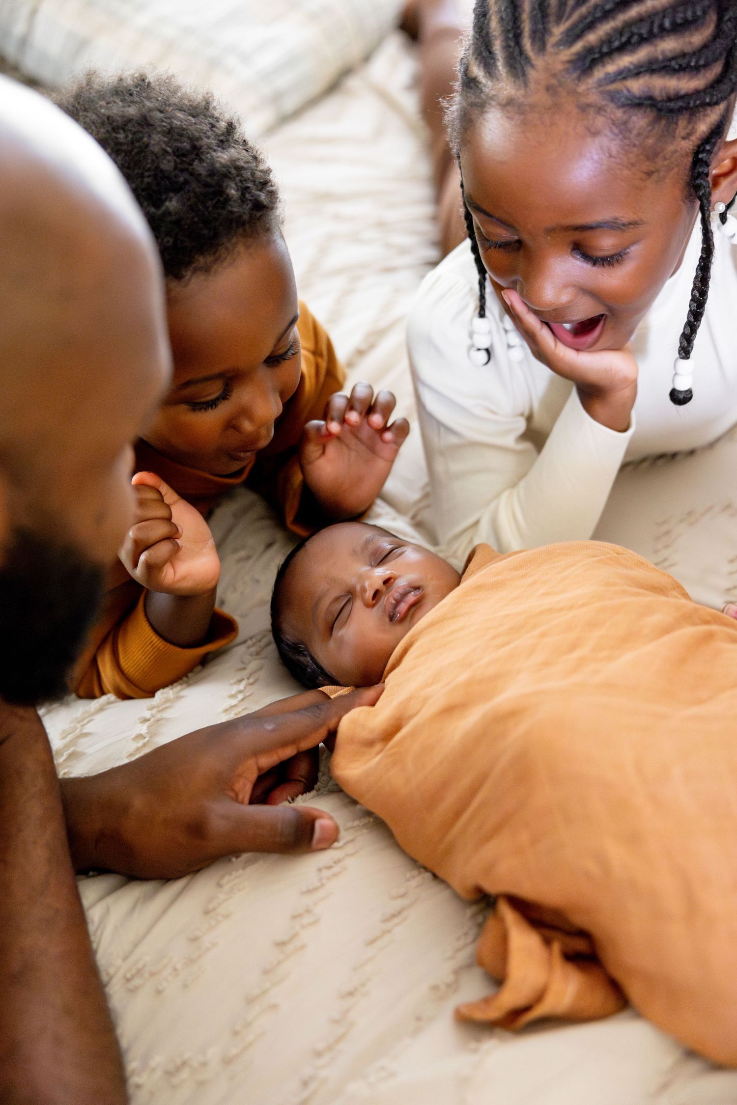 Family sharing tender moment with newborn baby on bed.