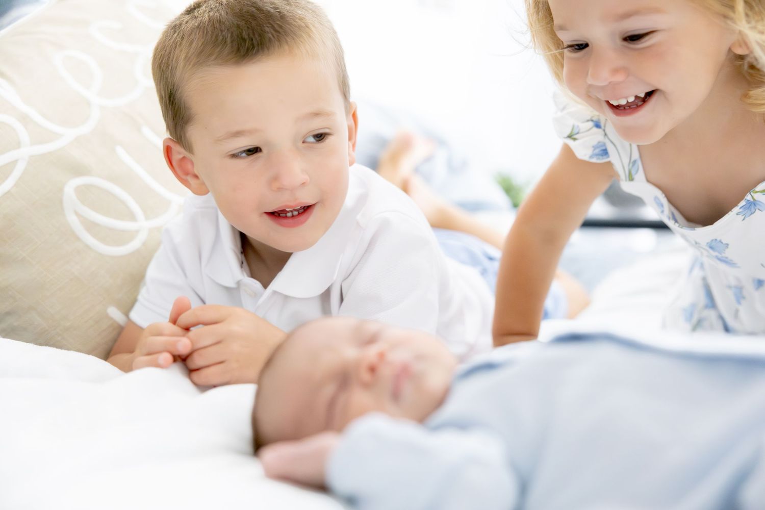 Children looking with wonder at newborn sibling on bed.