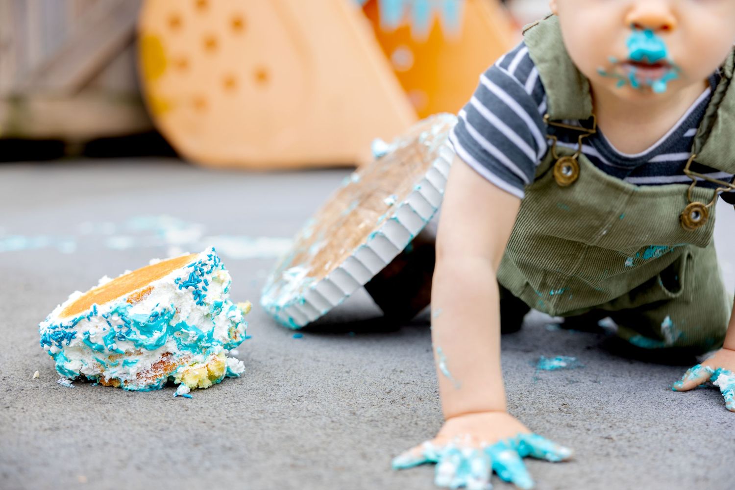 A messy overturned cake and the blue frosting covered hands of the toddler that smashed the cake during a cake smash session.