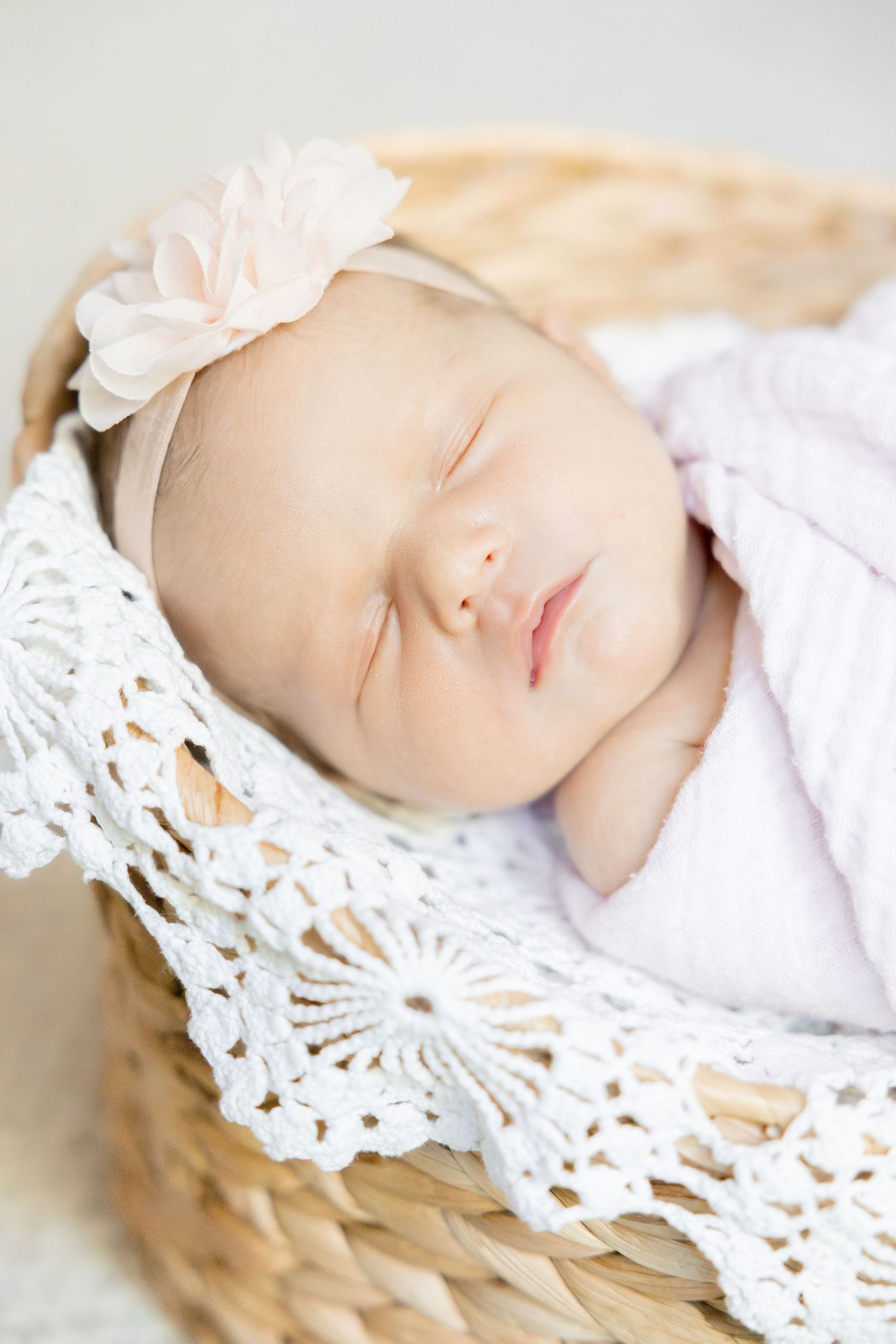 Sleeping newborn wrapped in delicate lace with pink flower accessory.