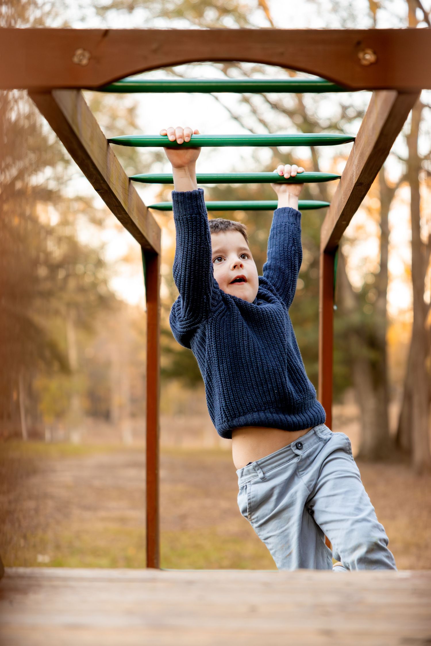 Young child in a navy sweater demonstrates impressive skills on monkey bars at a park during sunset.