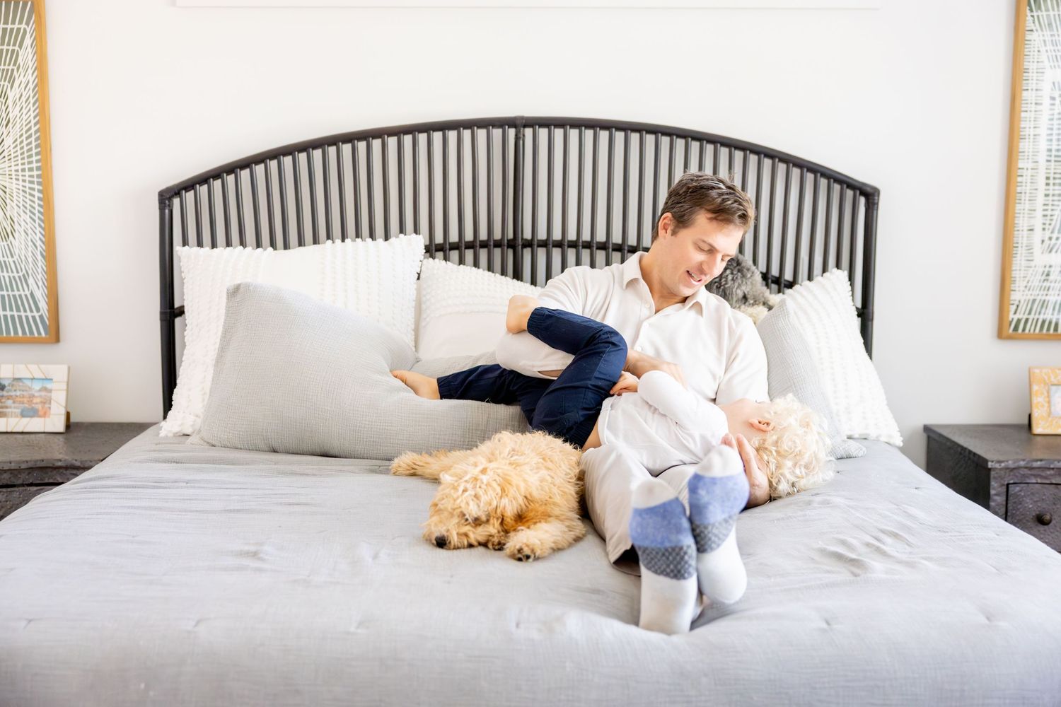 Family relaxing on a bed with their golden retriever in a bright bedroom.