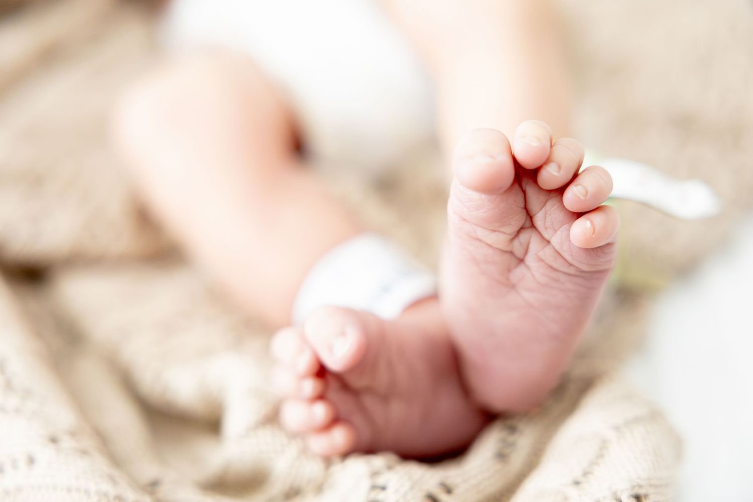 Close-up photo of tiny newborn baby feet on soft beige blanket.