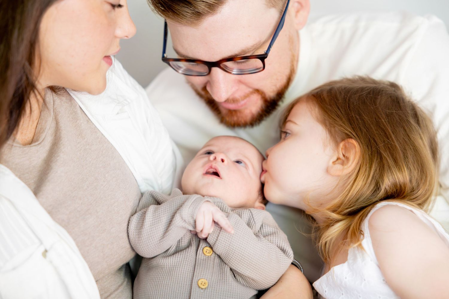 Intimate family portrait with baby in gray onesie surrounded by loved ones.
