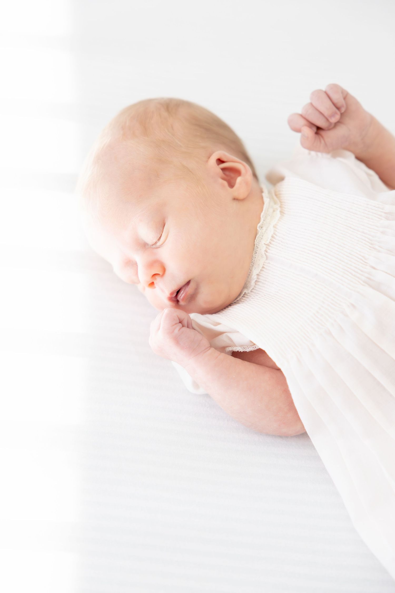 Sleeping newborn in white knit clothing against light background.