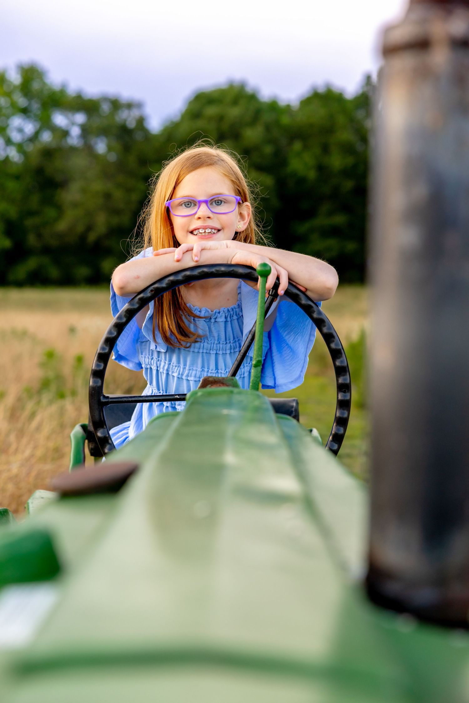 View over the hood of a green tractor during a playful countryside photo session at Blue Hill Garden in Monroe, NC.