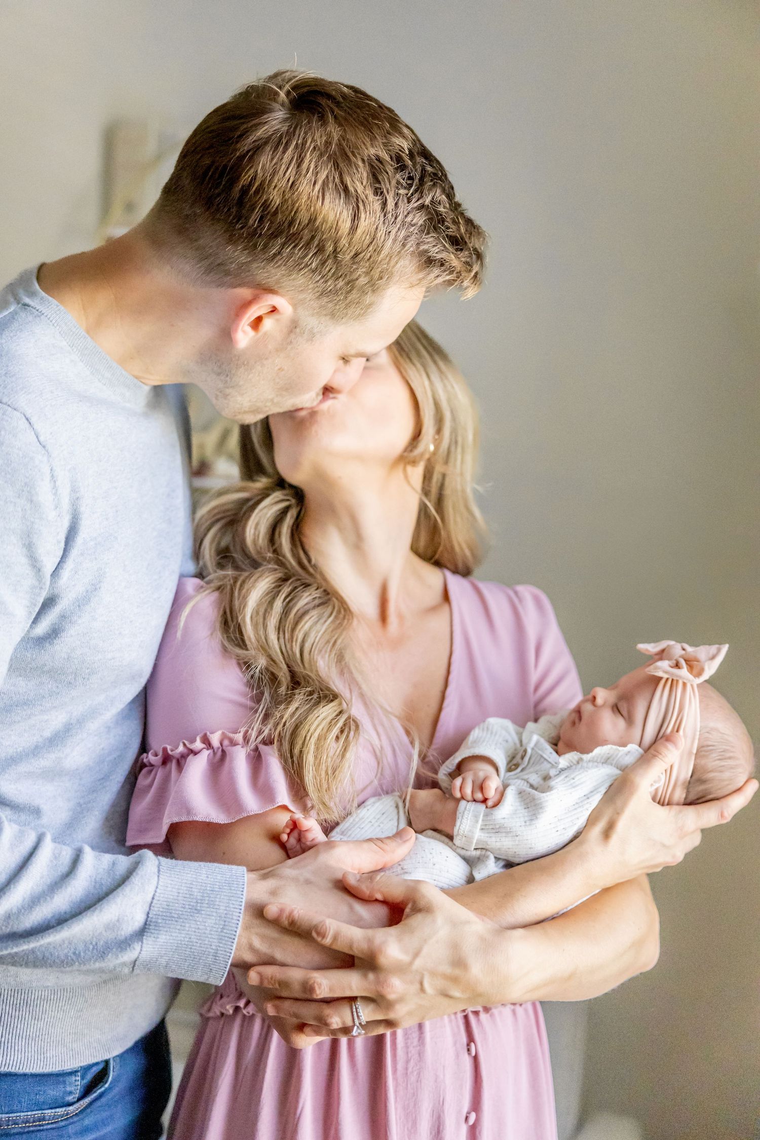 Parents in casual attire lovingly embrace their newborn baby during an indoor photoshoot.