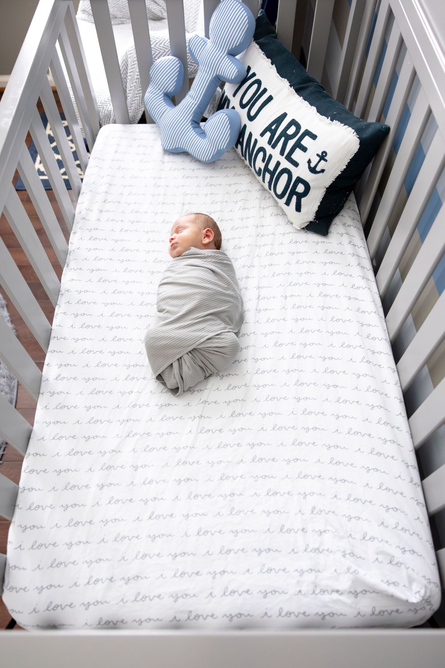 White crib with text-patterned bedding and decorative blue pillows.