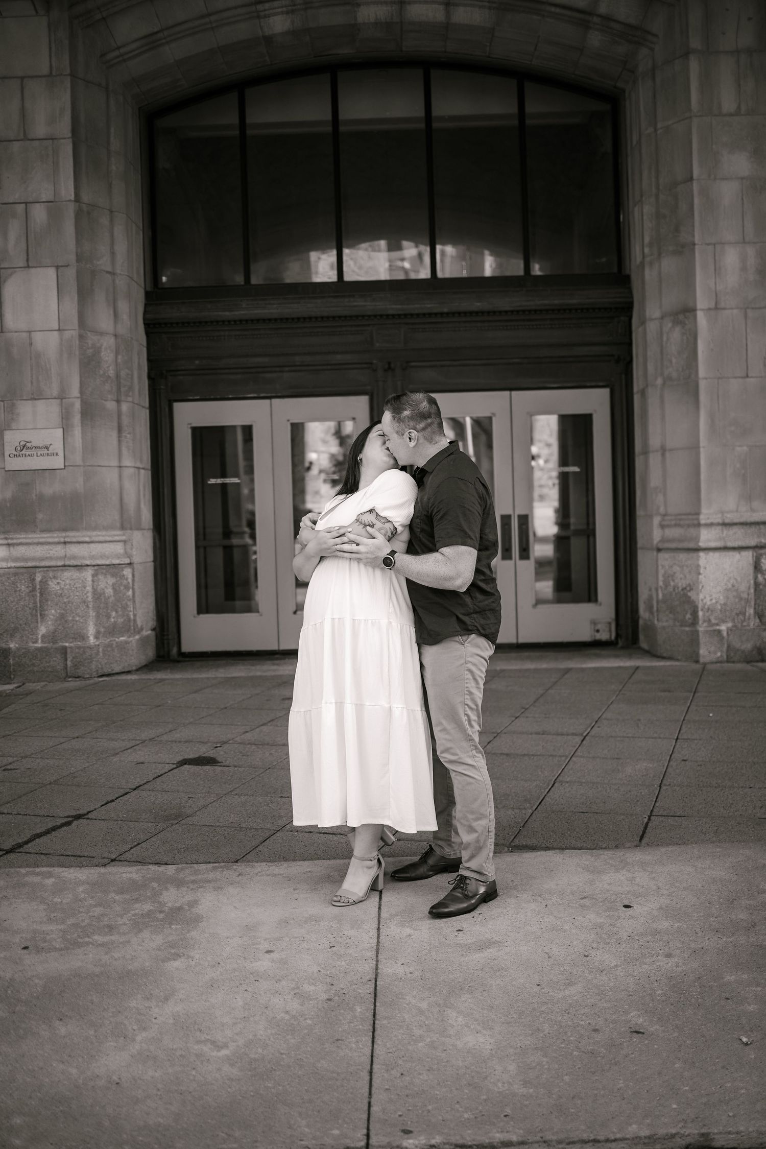 Black and white photo of a couple embracing and kissing in front of a stone building entrance.