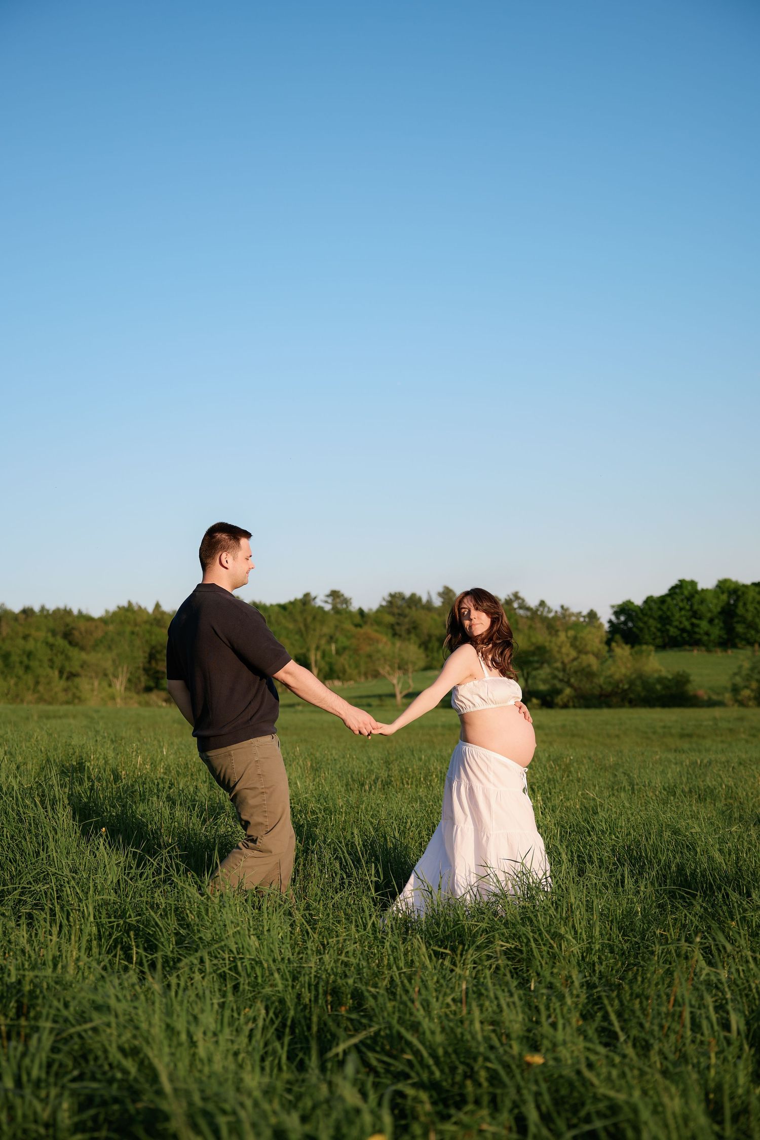 A couple dances together in a lush green field during golden hour.