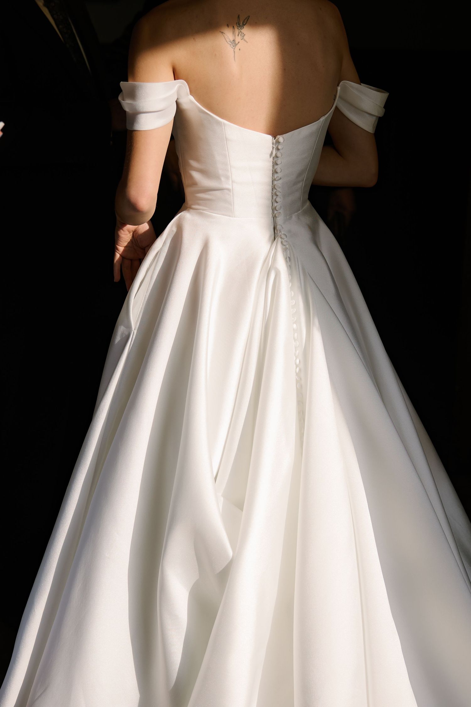 Close-up back view of a white wedding dress showing buttons and off-shoulder details.