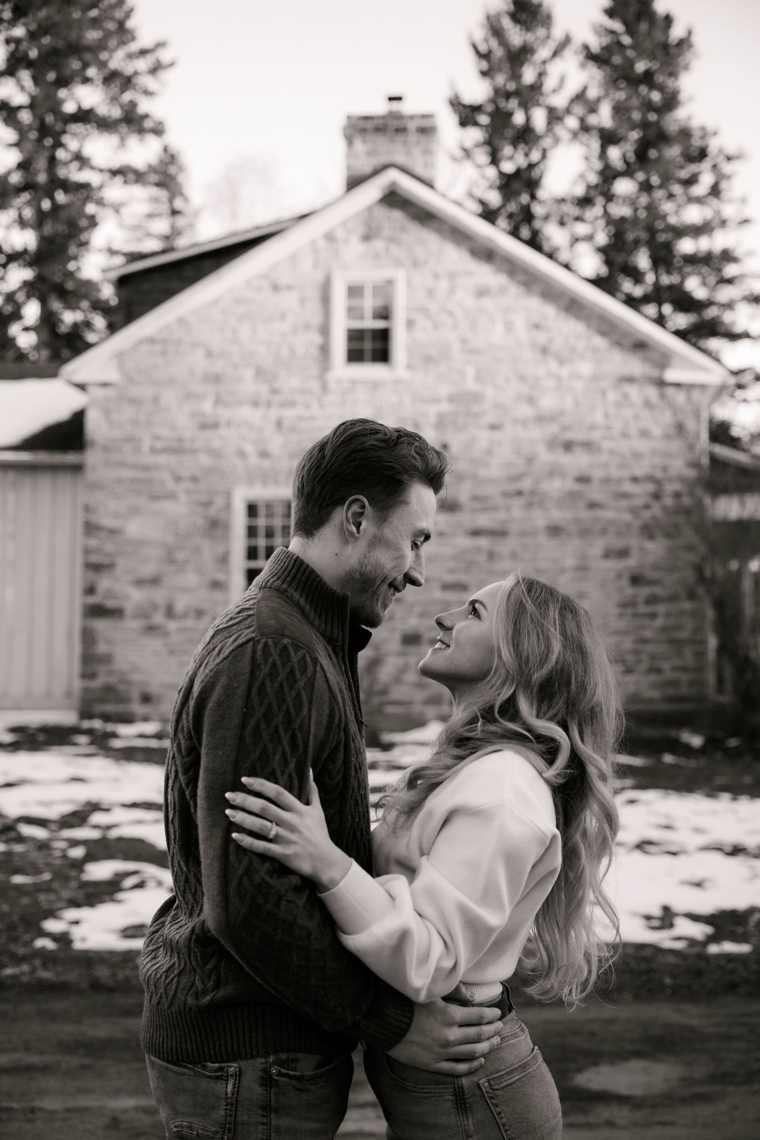 Intimate black and white portrait session outside rustic stone building in winter.