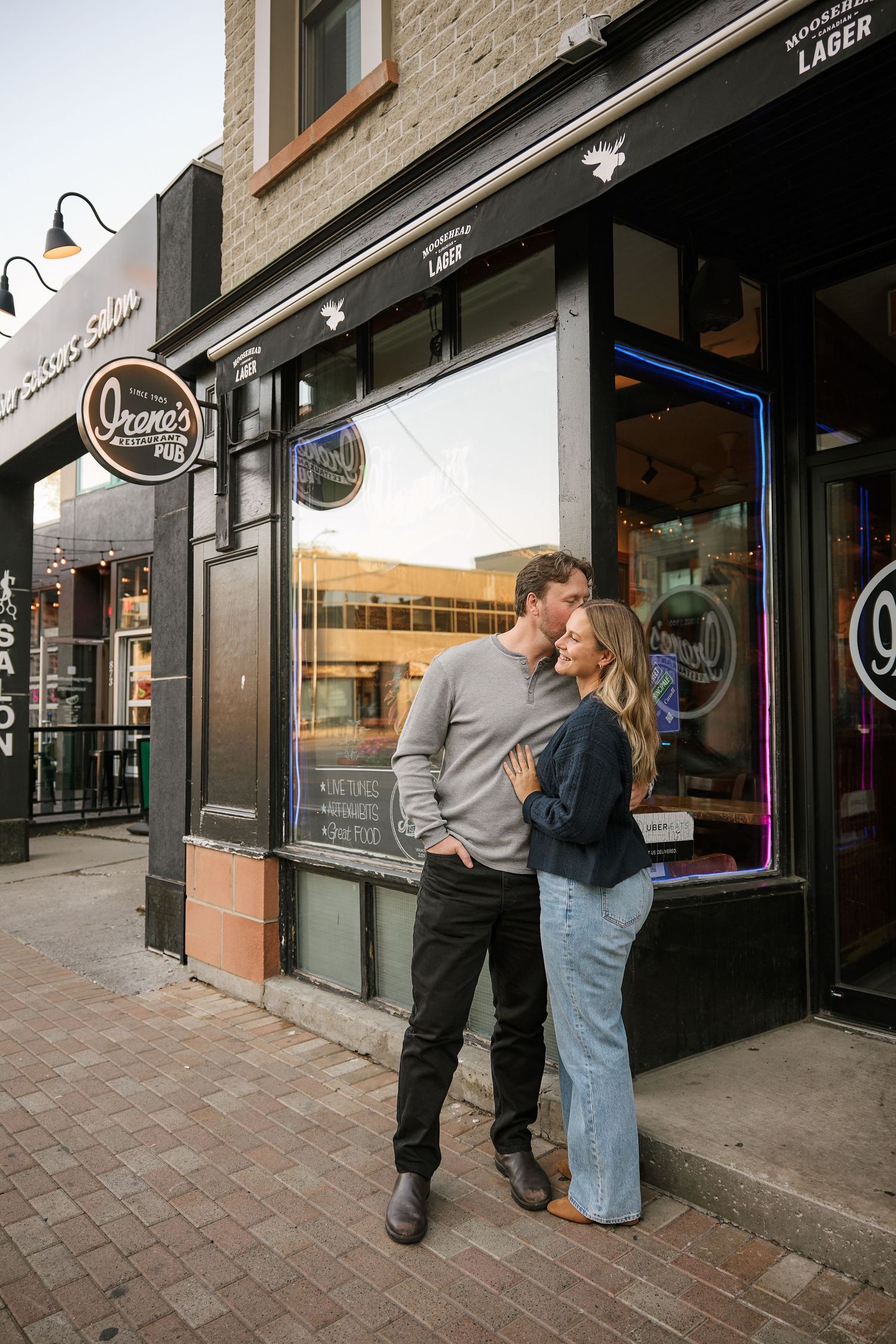 A couple sharing a romantic moment outside a storefront with vintage signage.