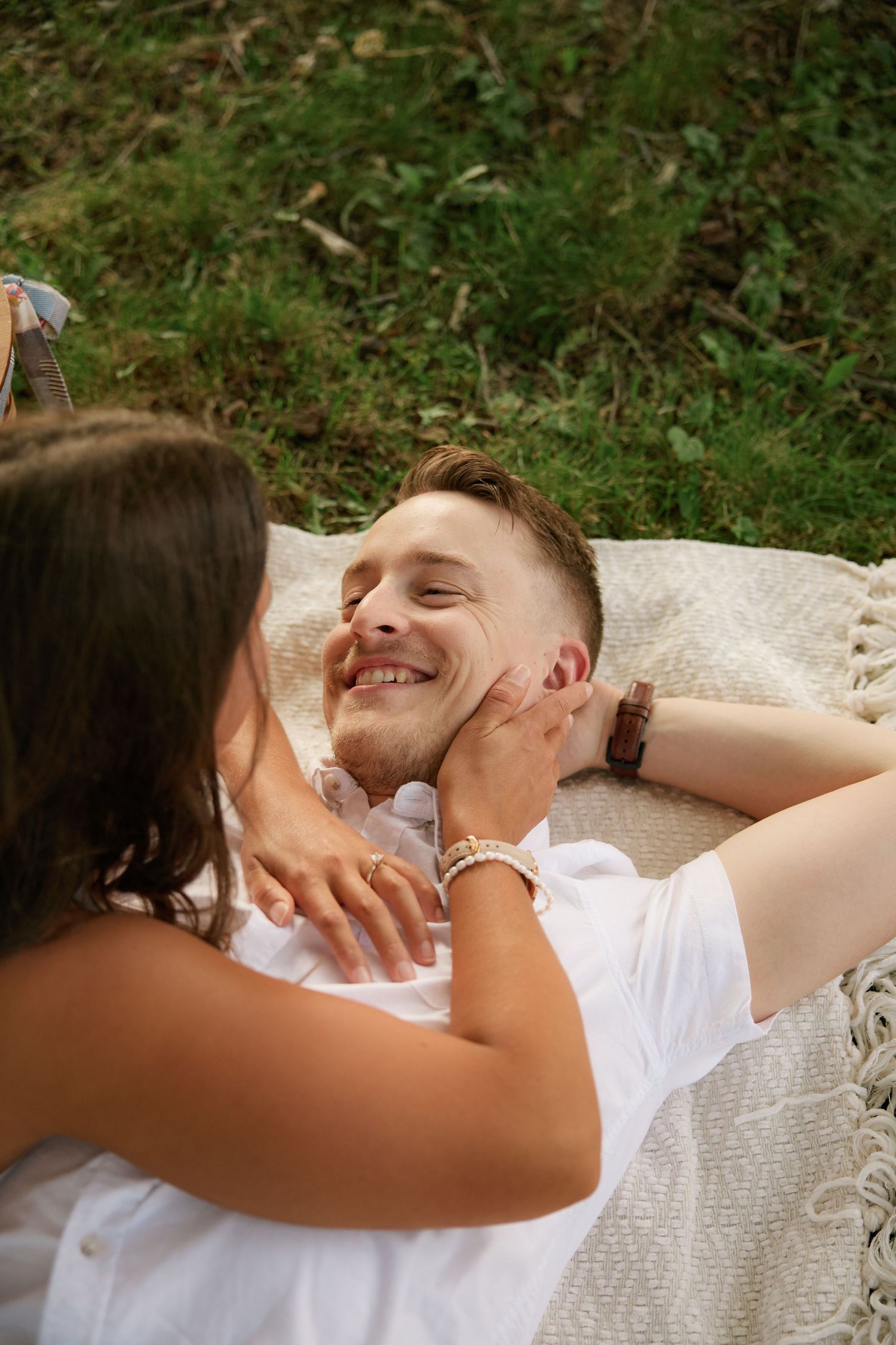 A couple shares an intimate moment while lying on a white blanket outdoors.