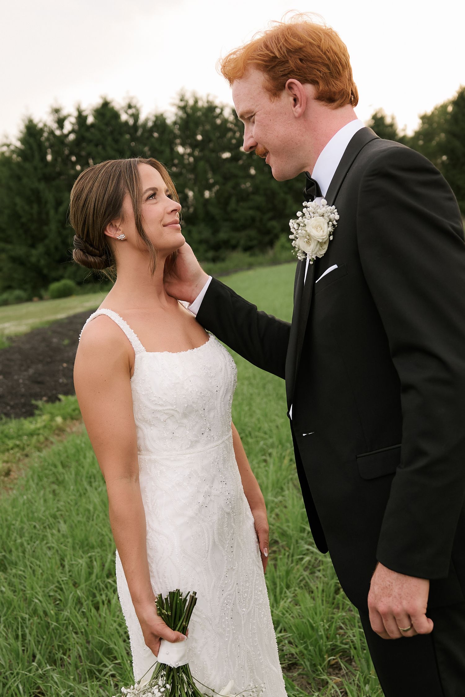 A tender moment between newlyweds standing in a grassy field.
