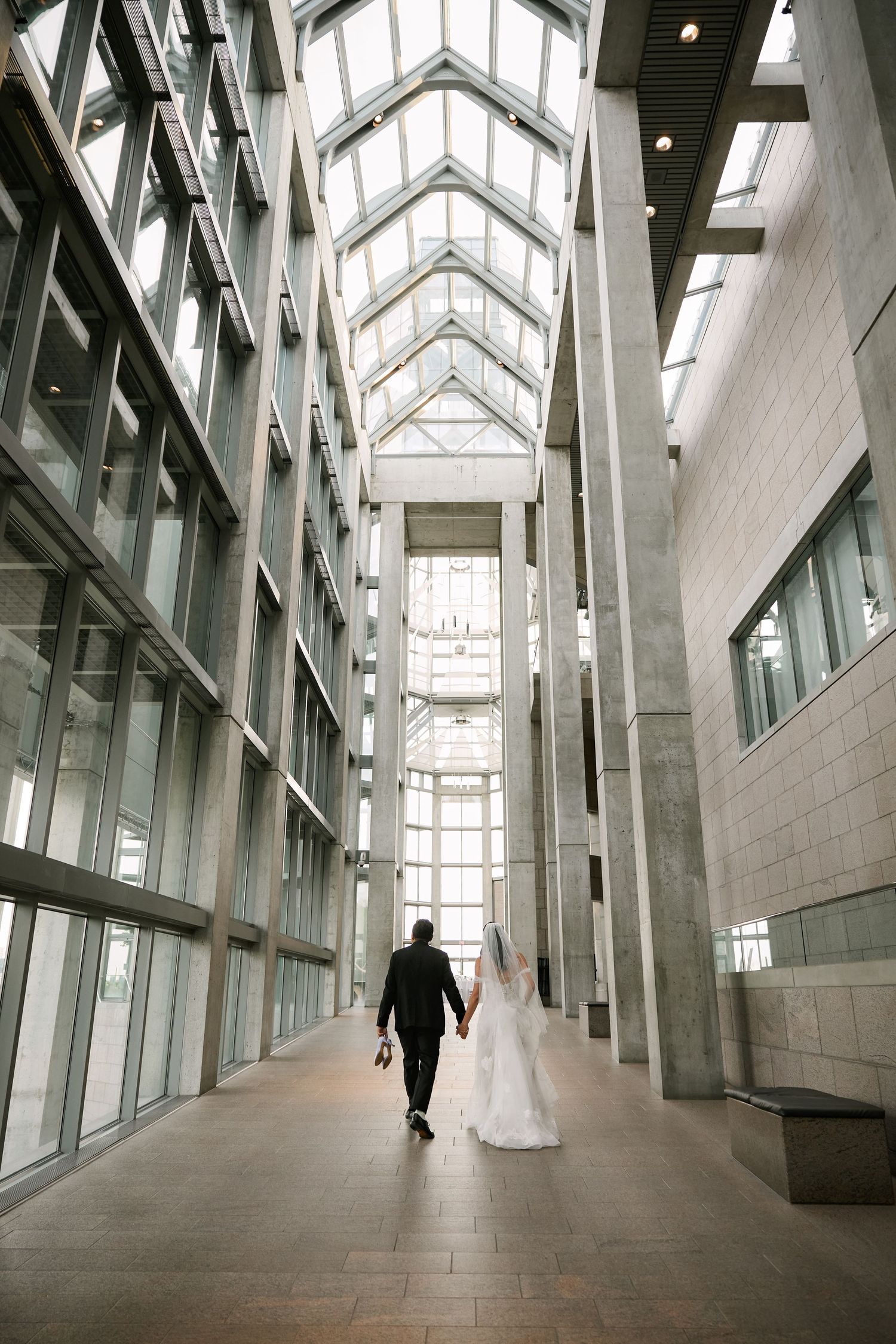 A couple walks down a modern architectural hallway with dramatic skylights and glass walls.