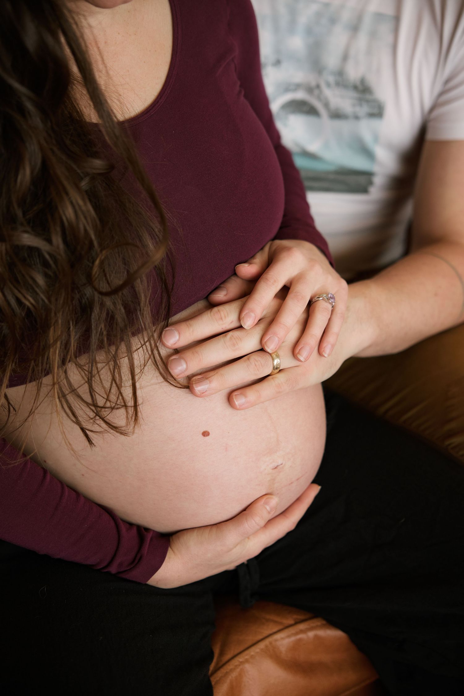 Close-up of hands resting on a pregnant belly with wedding rings visible.