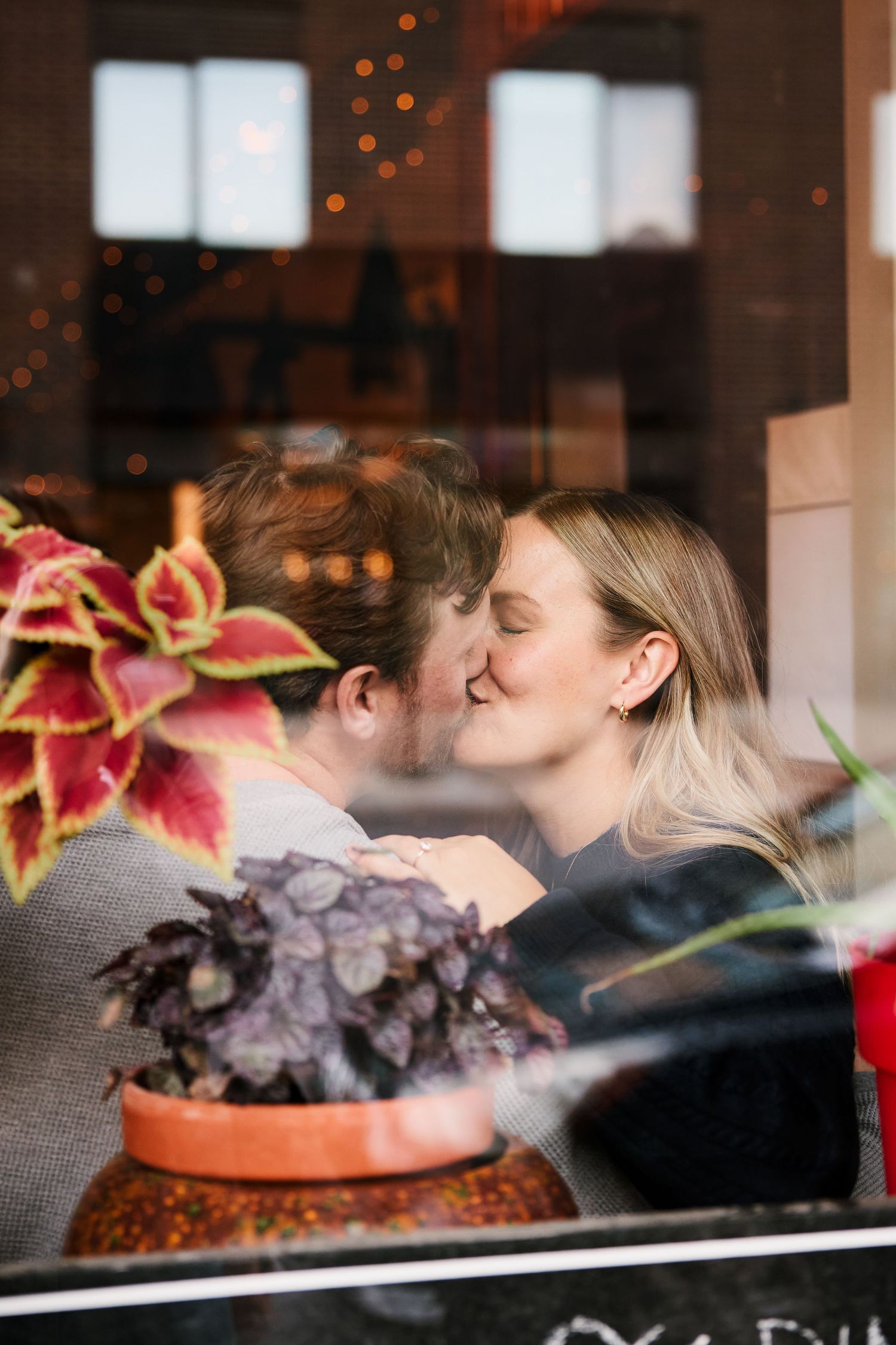 An intimate moment captured through a window with potted plants in the foreground.