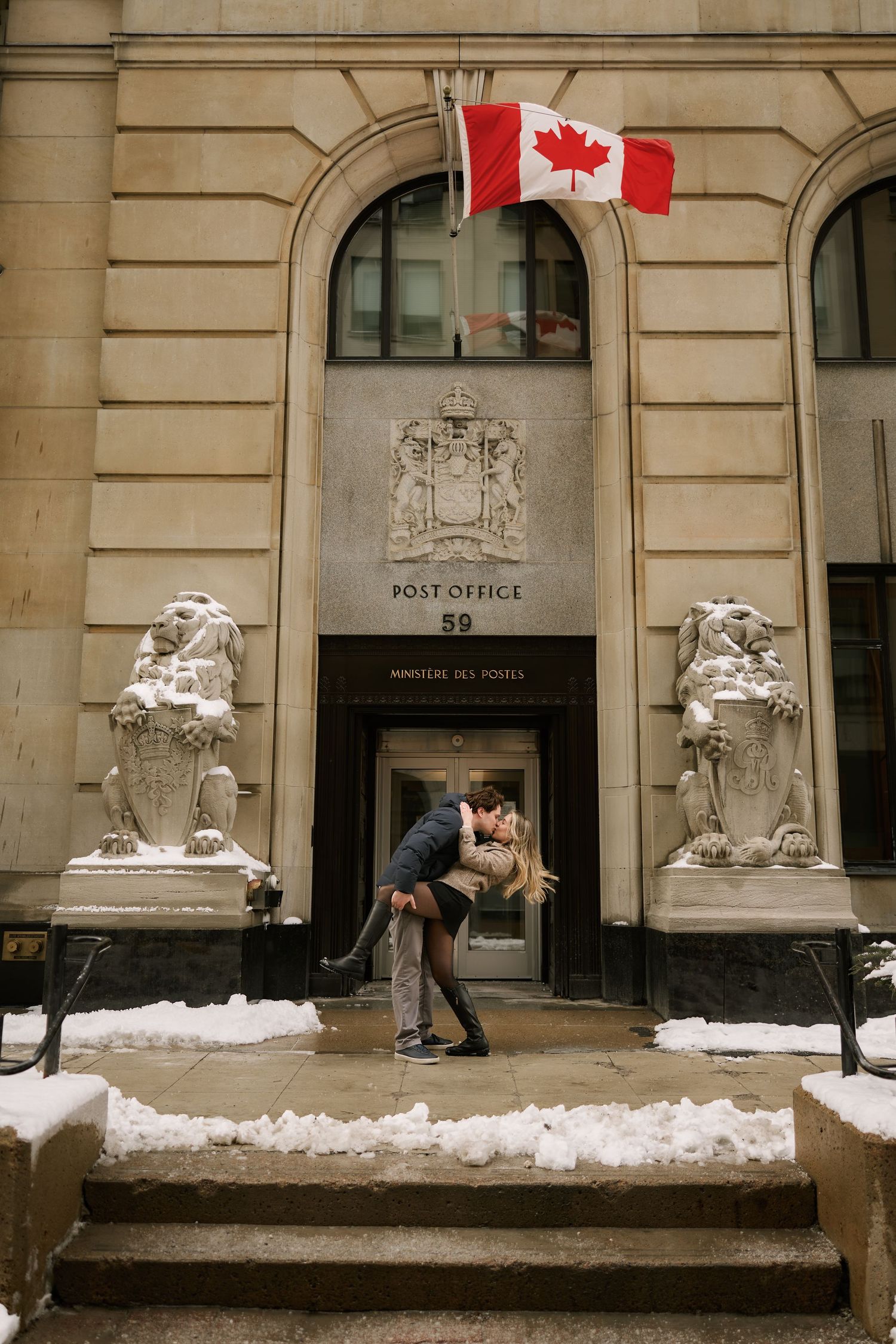 A romantic moment outside a Canadian post office building with stone lions and a maple leaf flag.