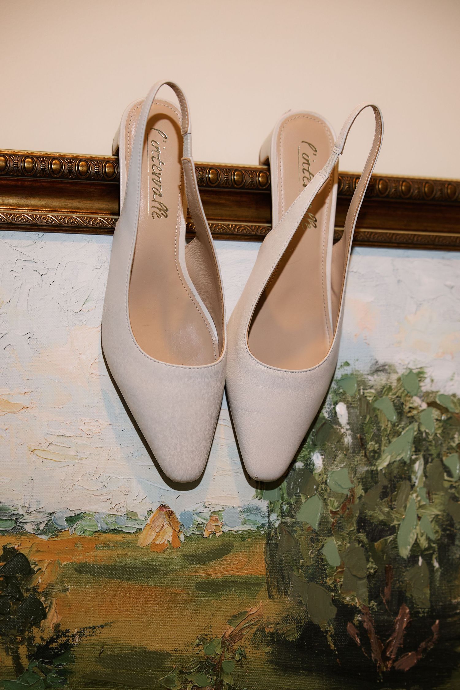 Elegant cream-colored slingback heels displayed on a painted landscape artwork.