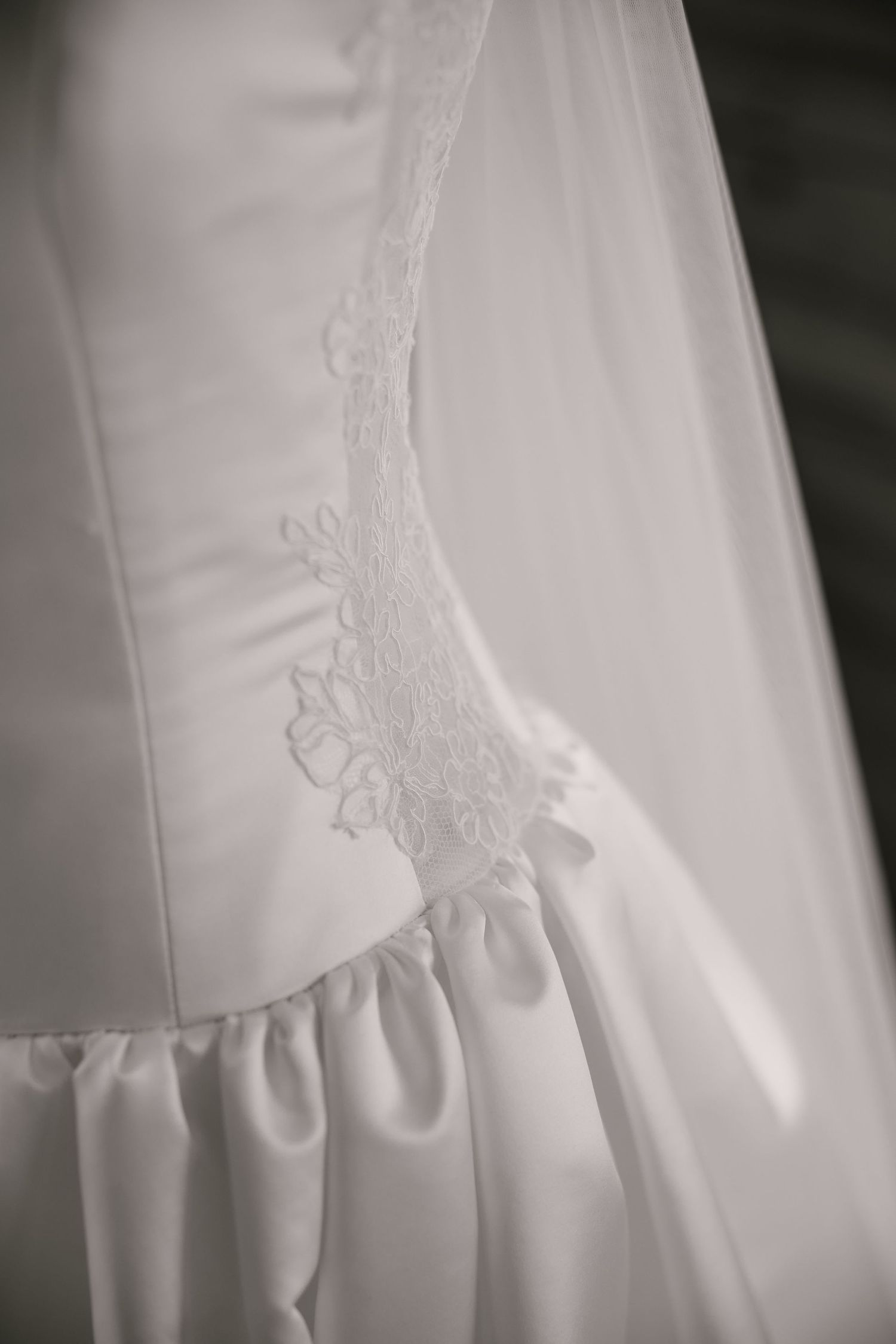 Close-up detail of white wedding dress showing intricate lace embroidery and pleating.