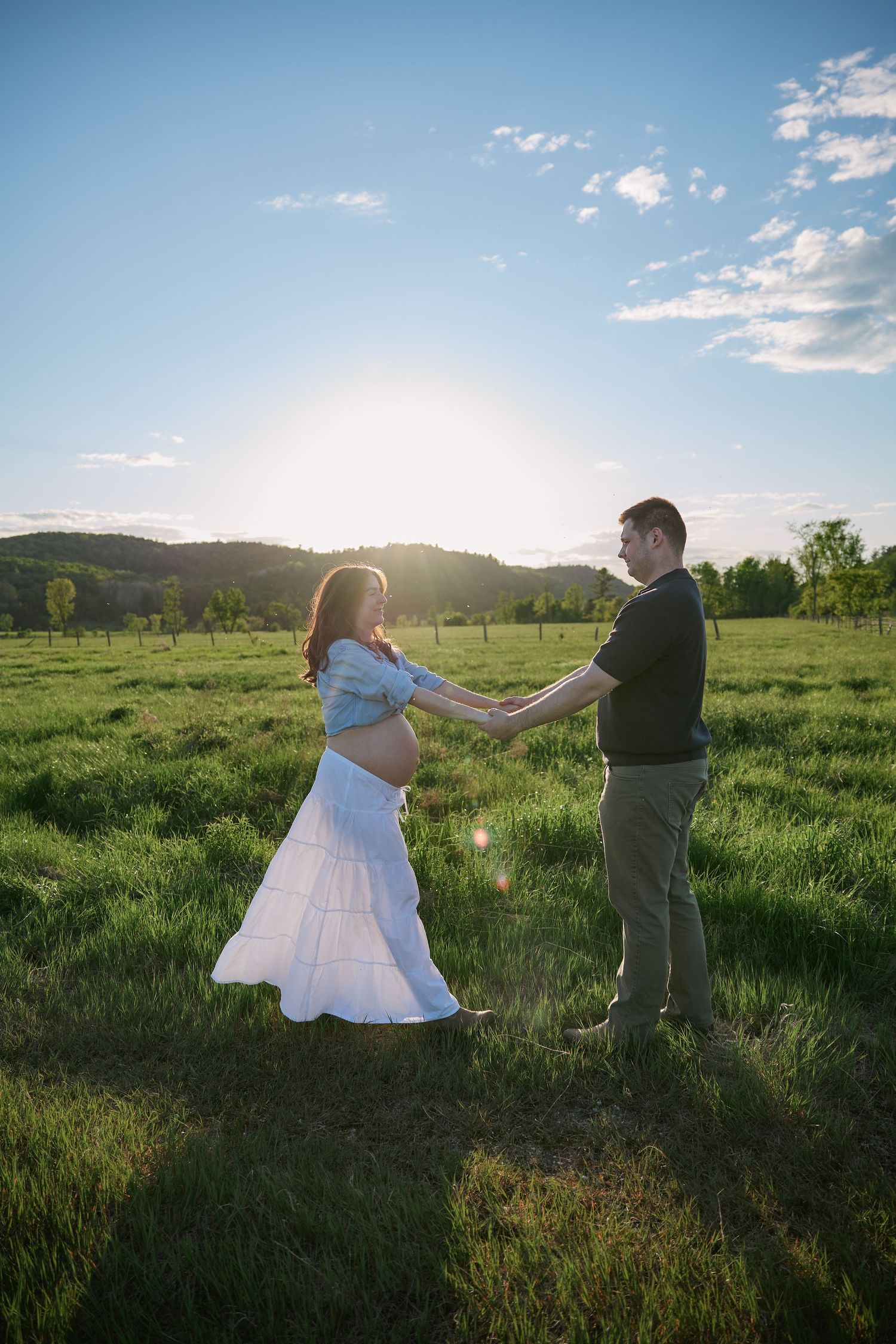 Two people hold hands in a green meadow during sunset.