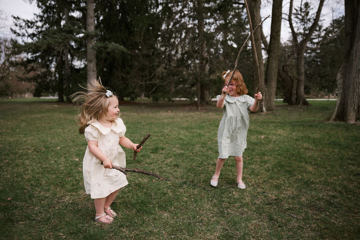 Two children in white dresses playing in a grassy park.