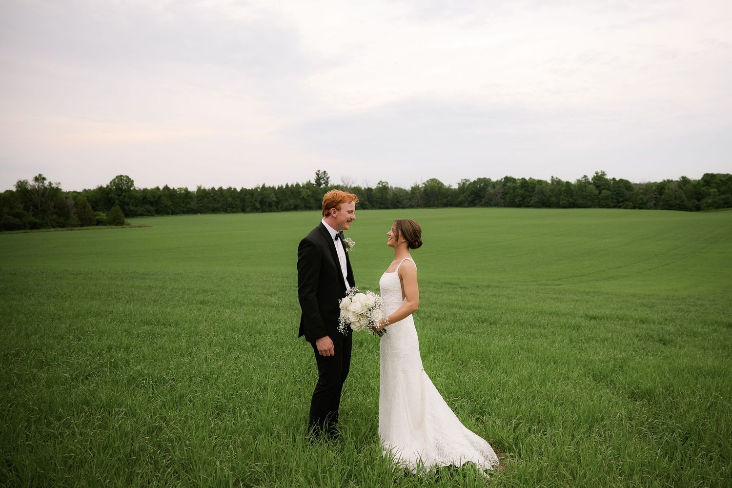 Newlywed couple walking together across a lush green field on their wedding day.