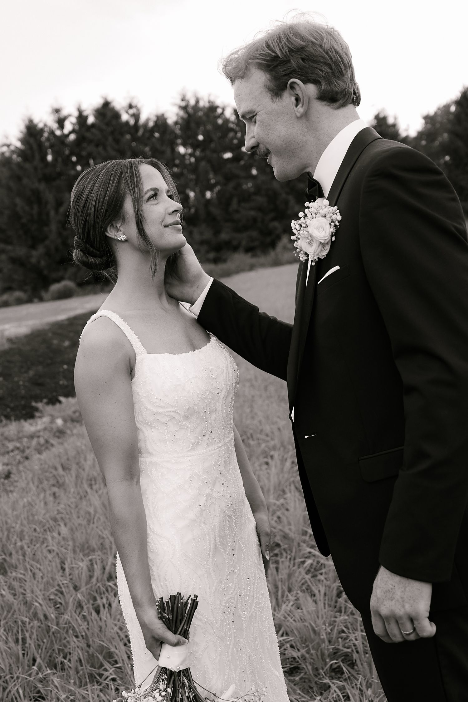 A black and white candid moment between newlyweds in a sunlit field.