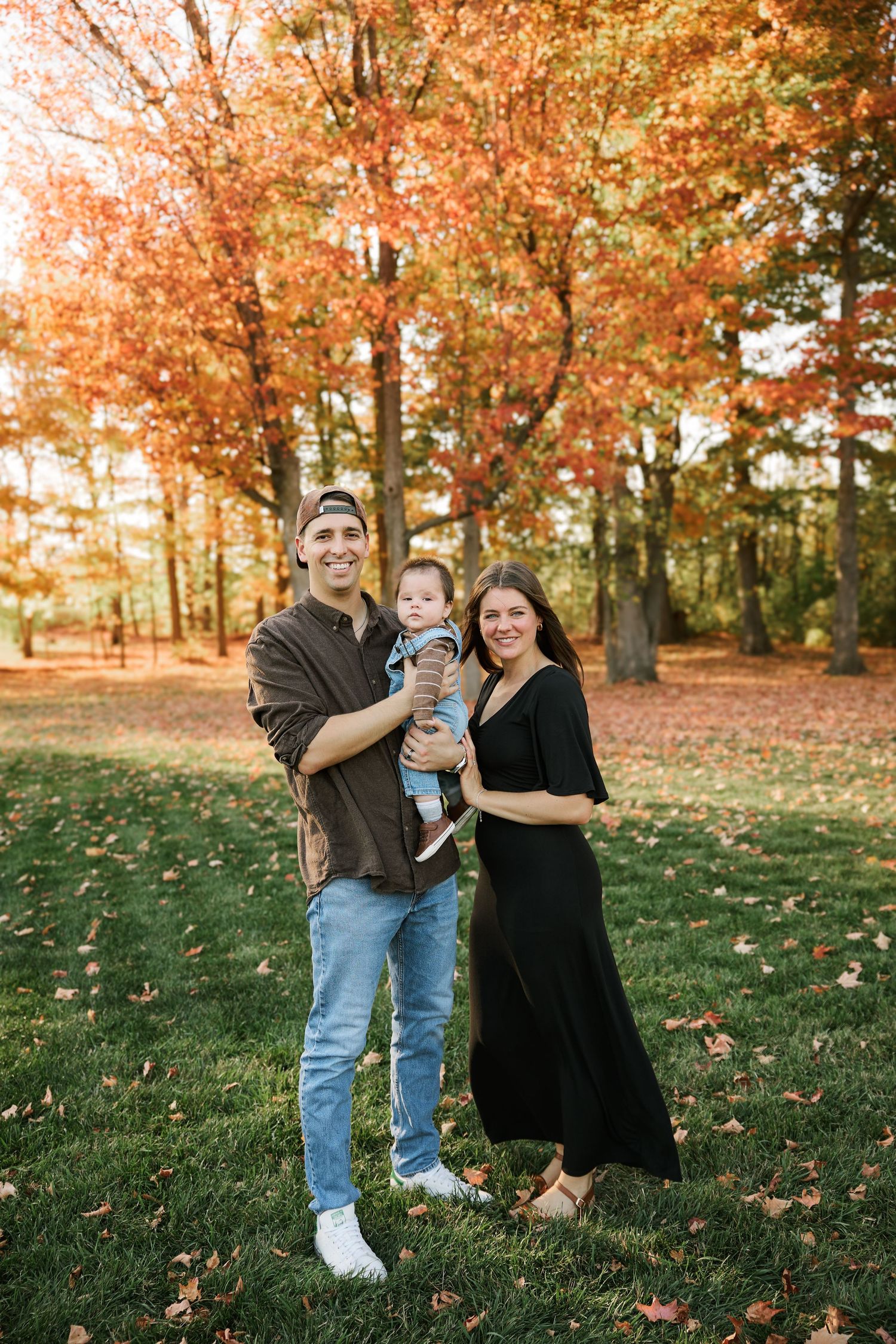 Family portrait session in park with beautiful fall colors and fallen leaves.