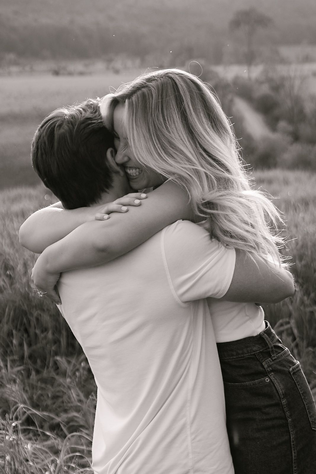 Black and white photo of a couple embracing in a field, smiling woman with long blonde hair hugging a man.