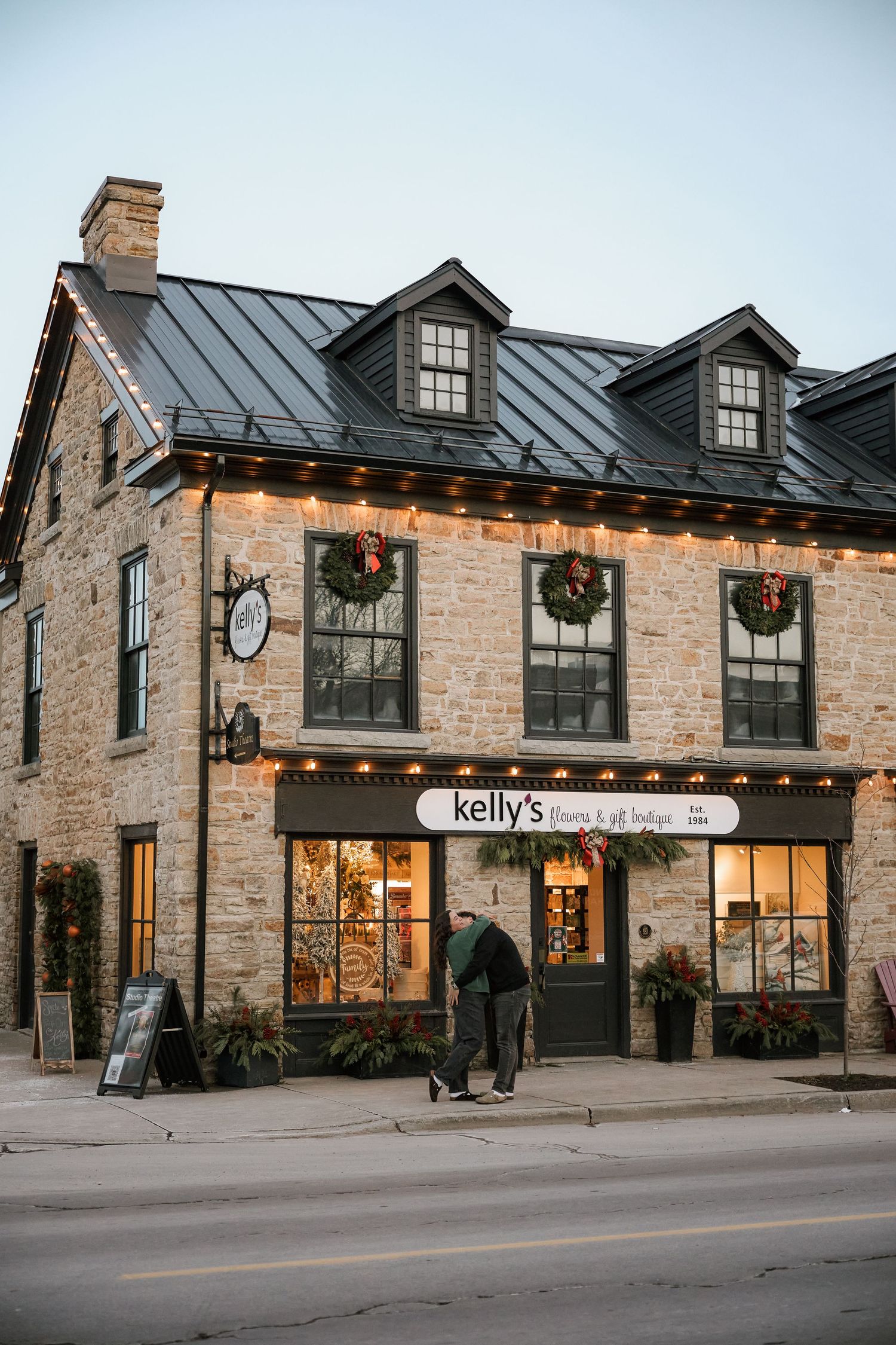 Charming stone building housing Kelly's Floral & Gift Boutique decorated with Christmas wreaths and string lights at dusk.