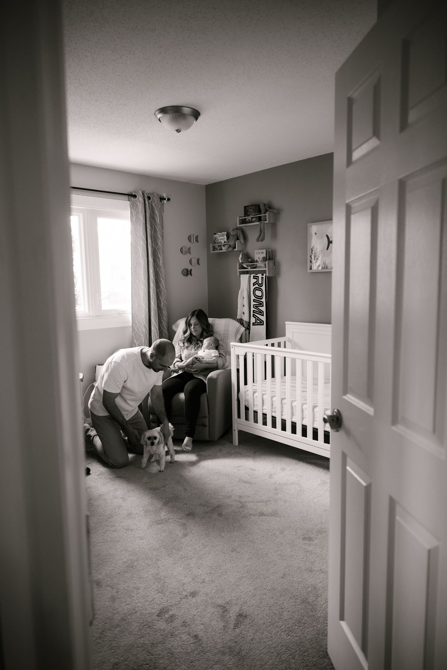 Black and white nursery scene with a crib and people gathered near a window.