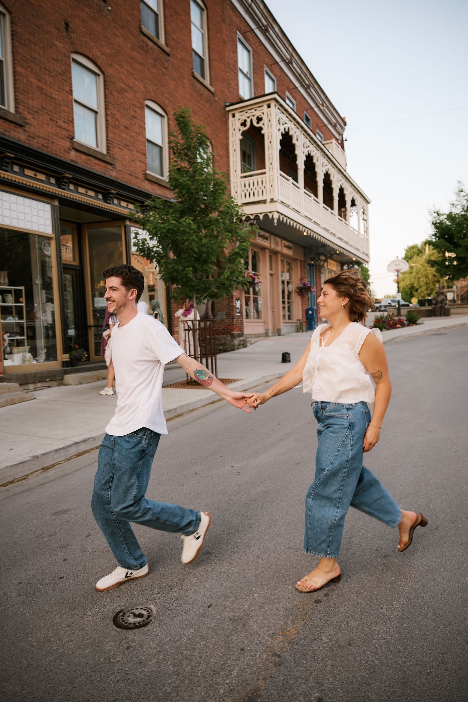 Happy couple holding hands and walking across a street in a charming historic town with brick buildings.