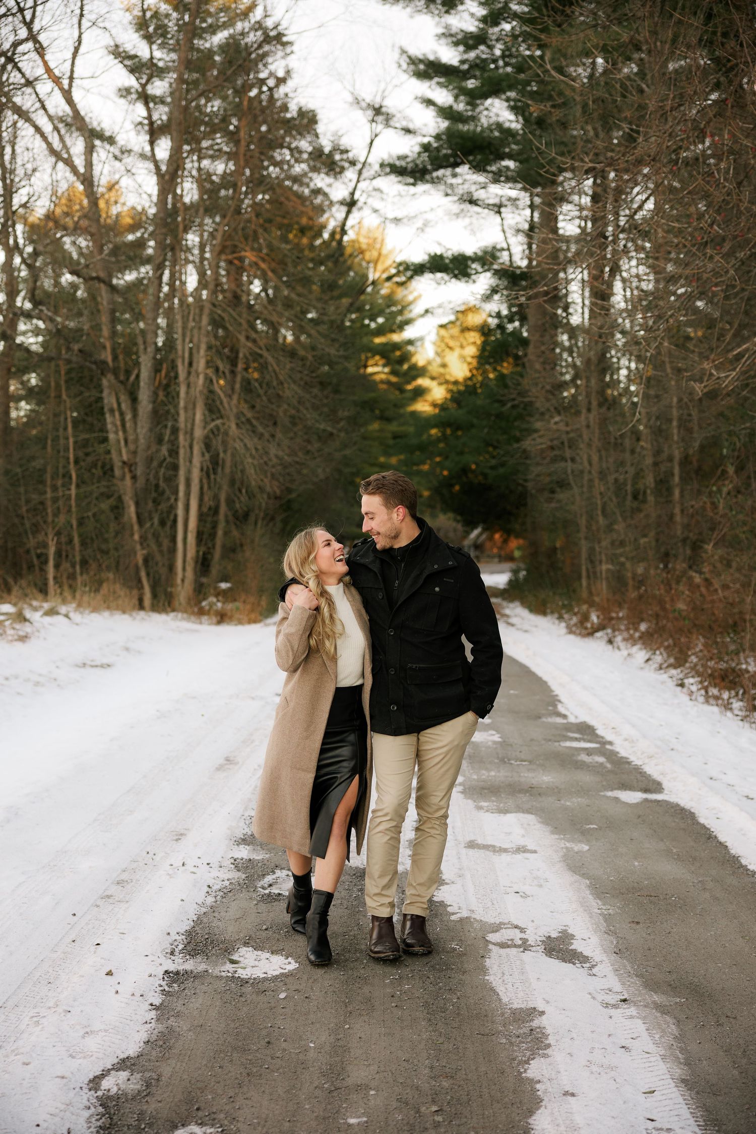 Couple sharing a romantic moment on a snowy forest road in winter, woman in beige coat and man in black jacket.