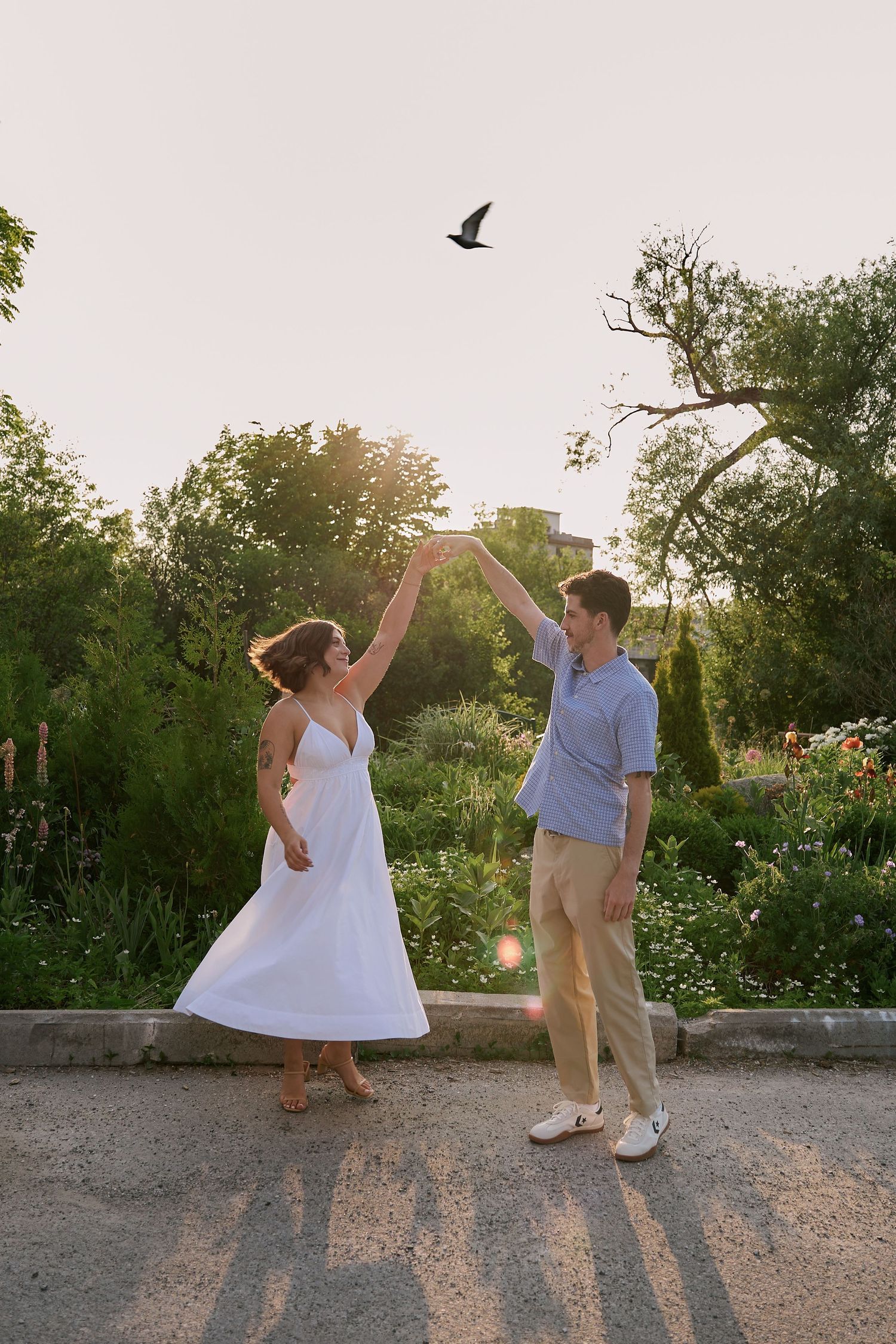 A couple dances together in a garden at sunset with a bird flying overhead.