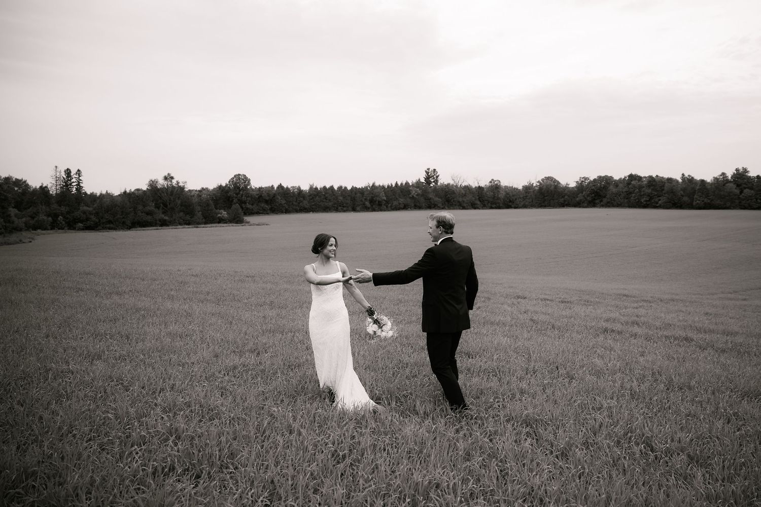 Black and white wedding photos captured in an open field with dramatic sky.