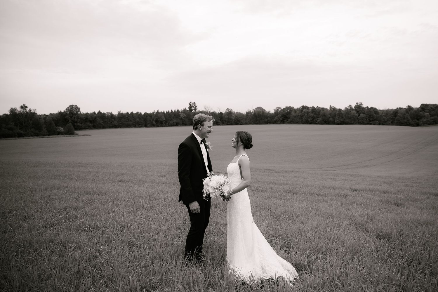 A black and white photo of a couple sharing an intimate moment in an open field.