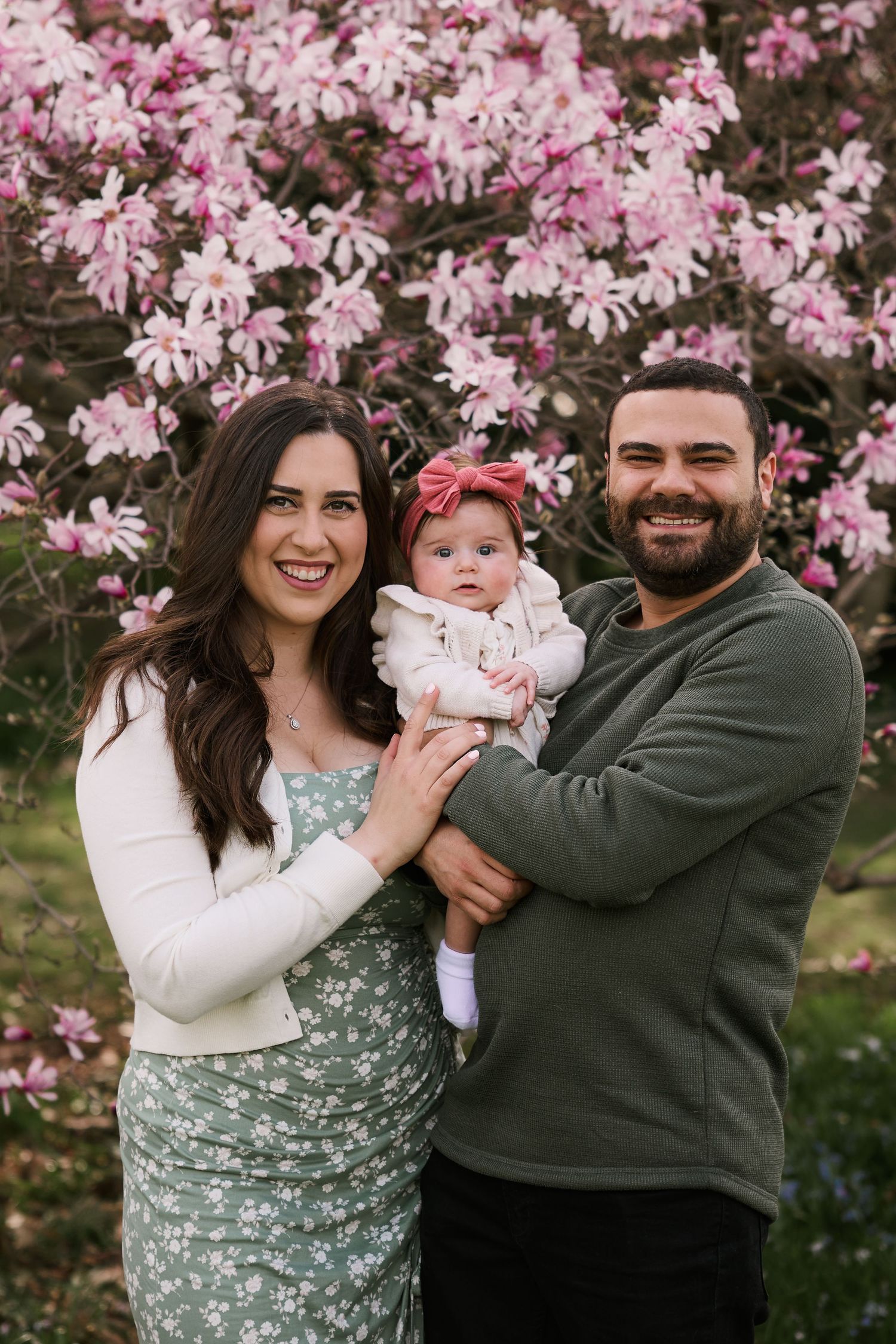 A happy family portrait captured against a backdrop of pink magnolia blossoms in full bloom.
