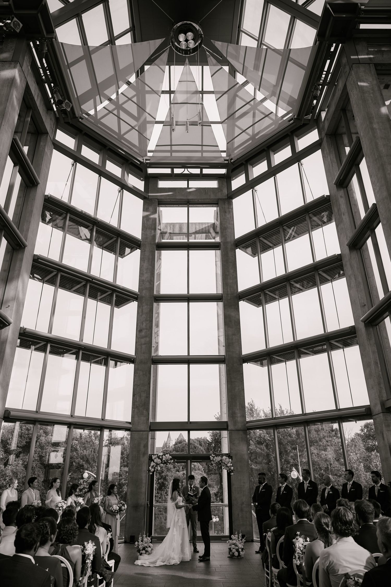 Modern glass atrium wedding ceremony venue with geometric ceiling and natural light streaming in.