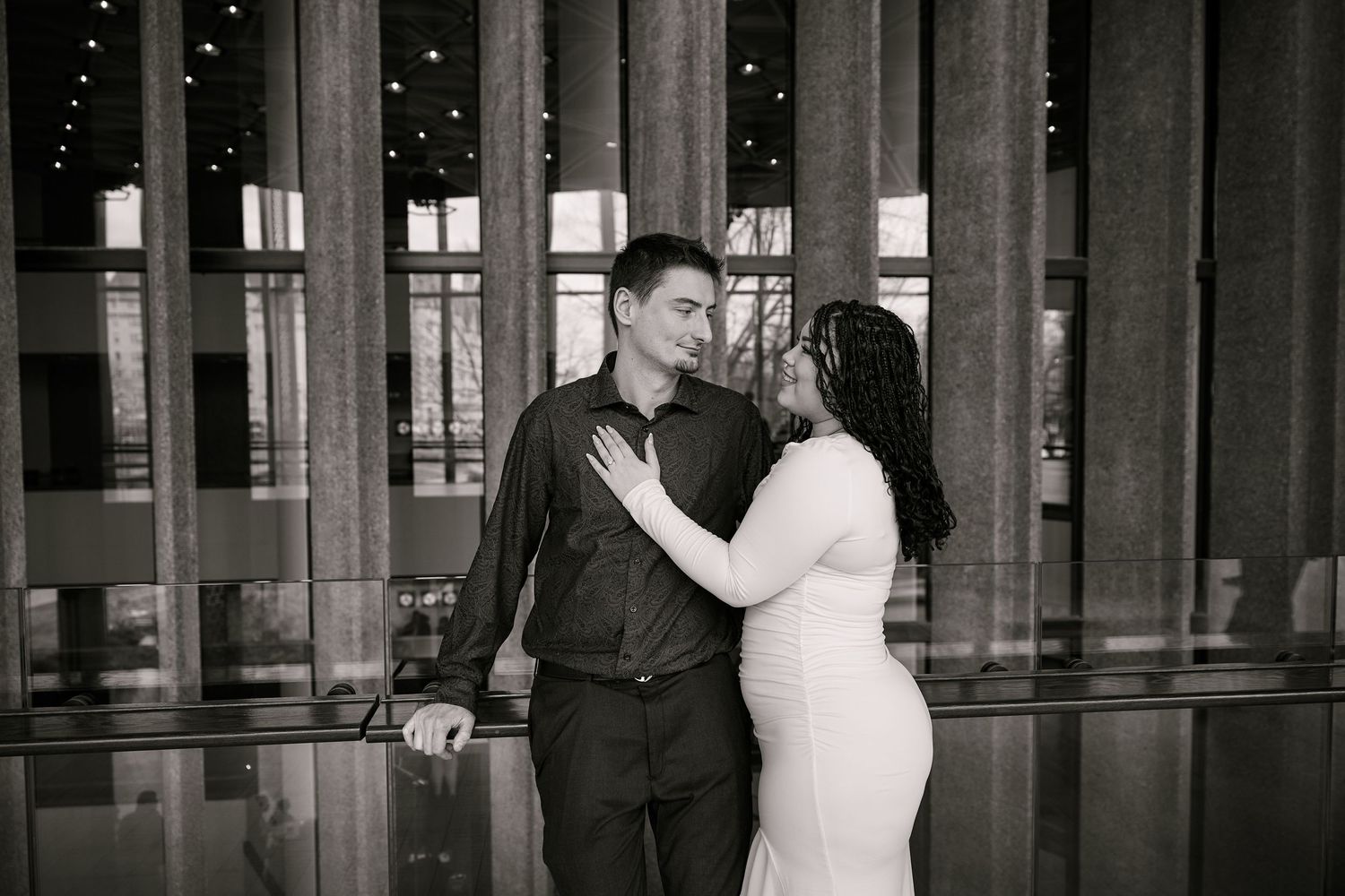 Black and white photo of a couple sharing a romantic moment in front of elegant columns at a formal venue.