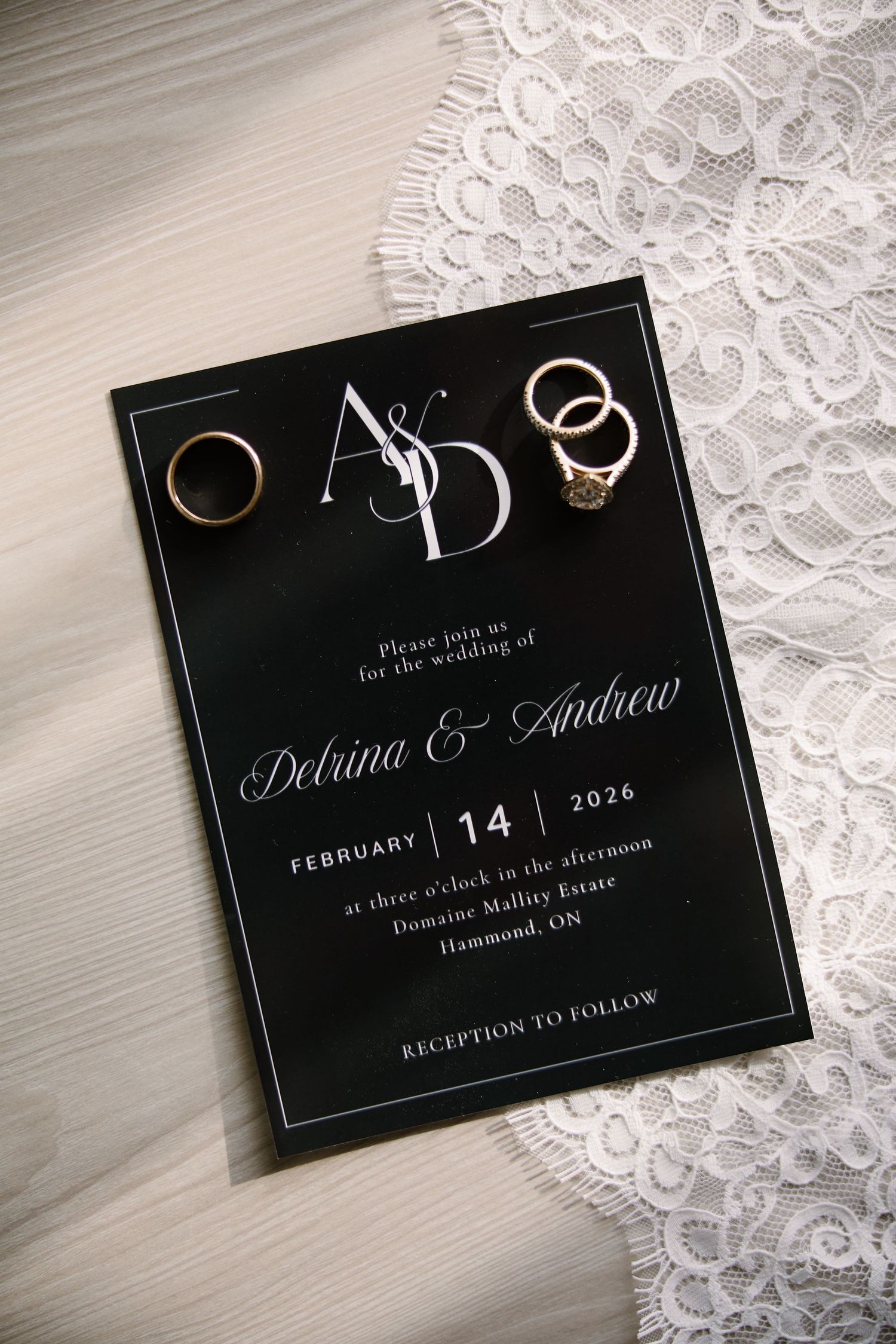 Elegant black wedding invitation for Delrina and Andrew, February 14 2026, with gold wedding rings at Domaine Mallity Estate.