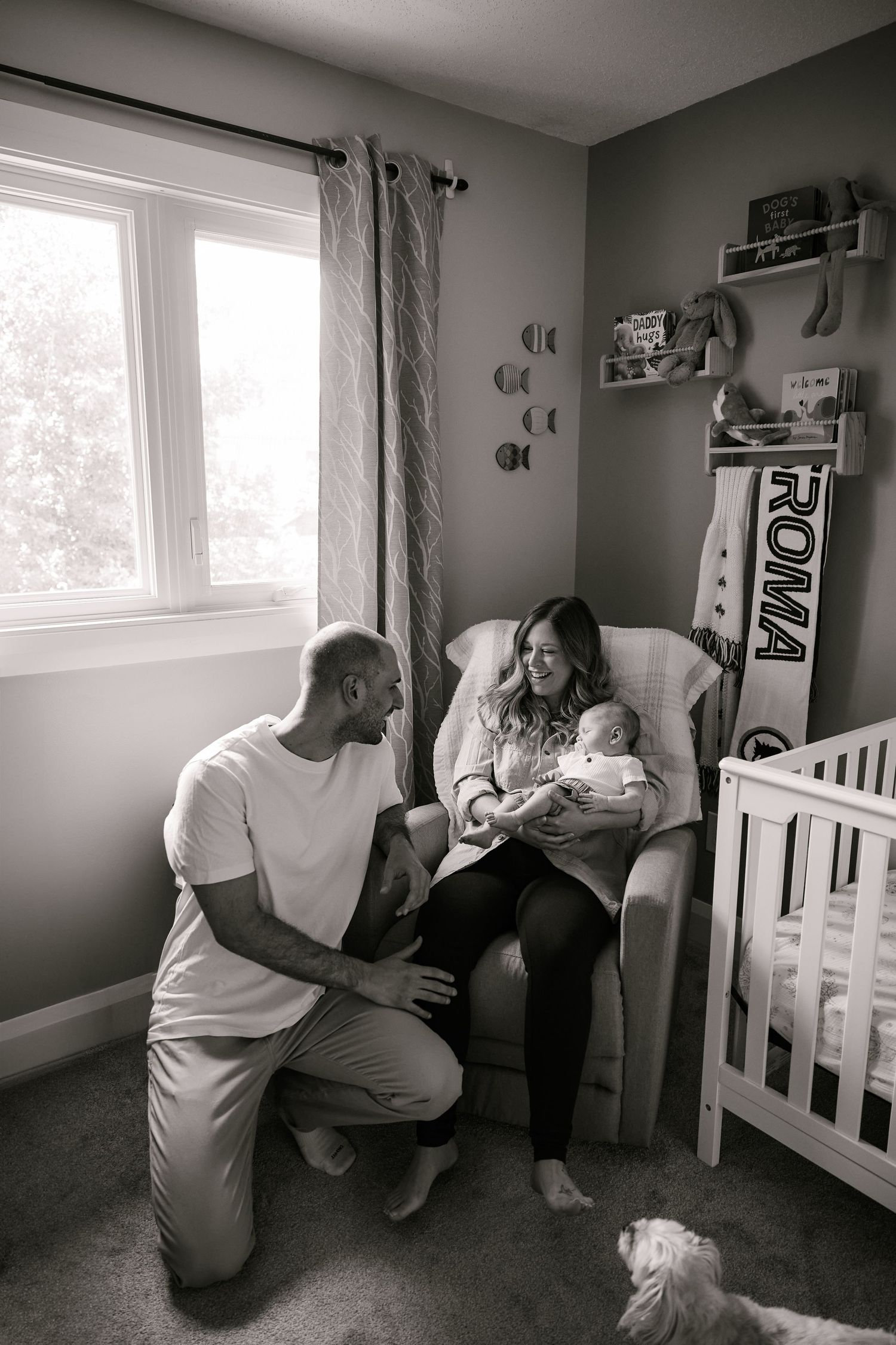 Black and white photo of a cozy nursery scene with a white crib and rocking chair.