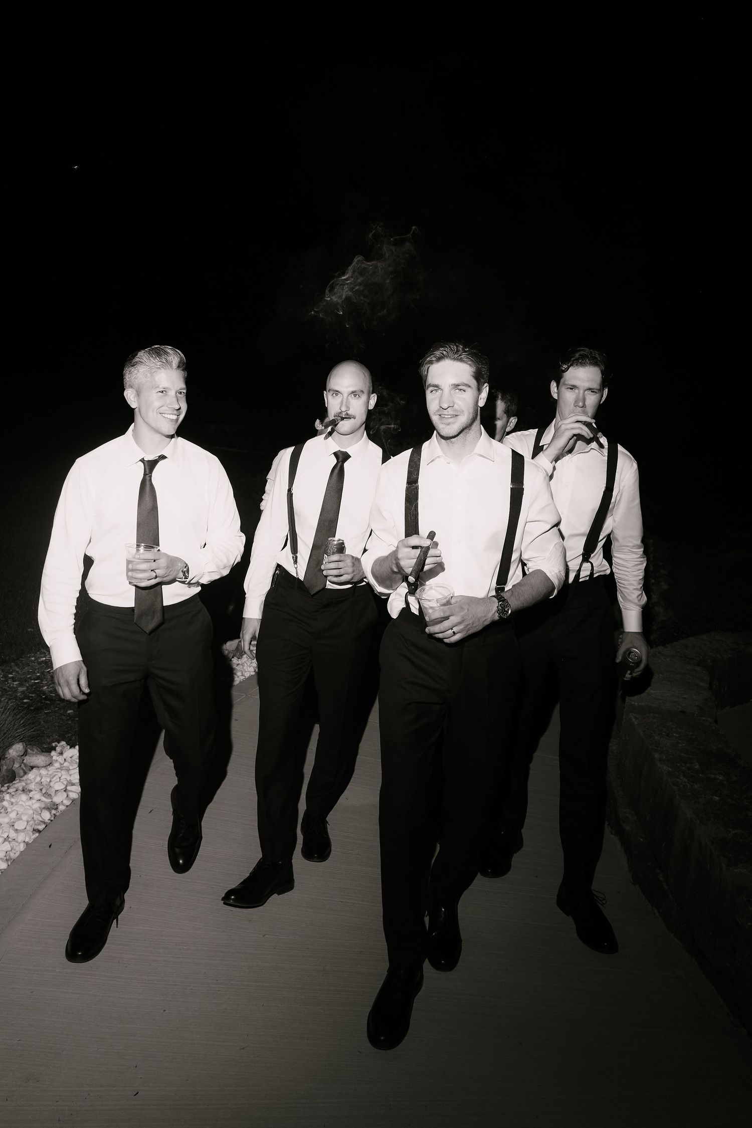 Black and white photo of four groomsmen in white shirts and ties walking confidently at a wedding reception.