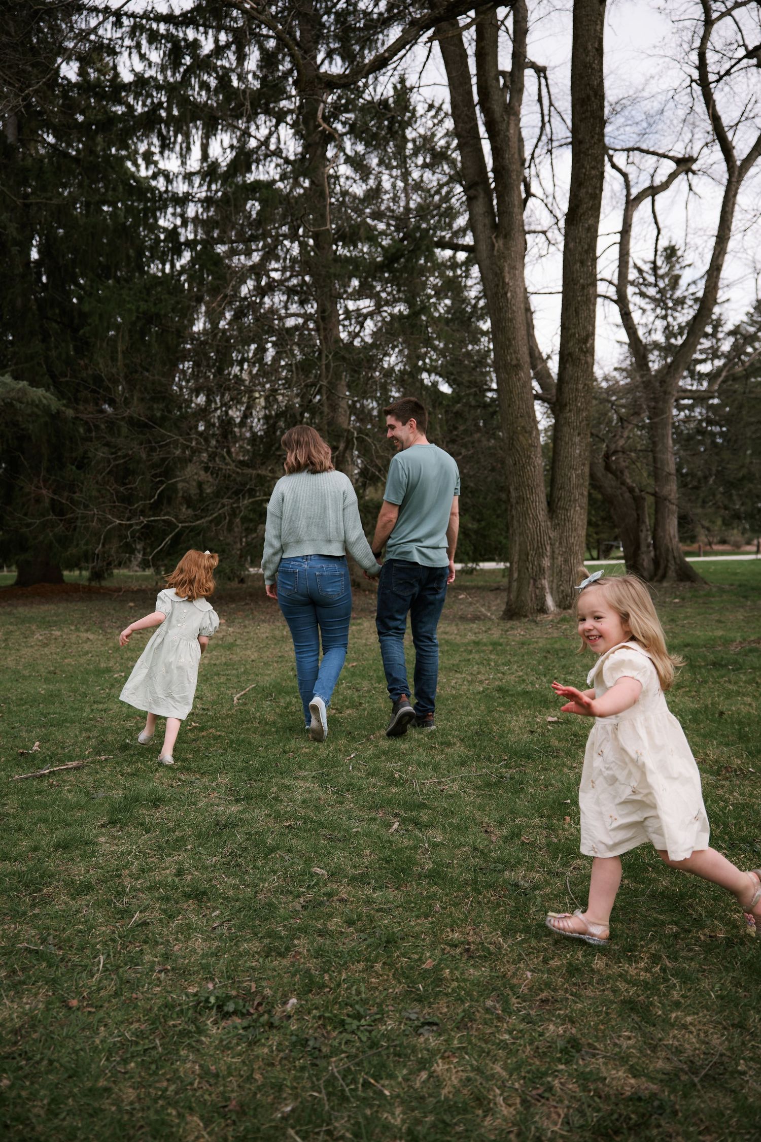 Family strolling through a wooded park with children in white dresses.