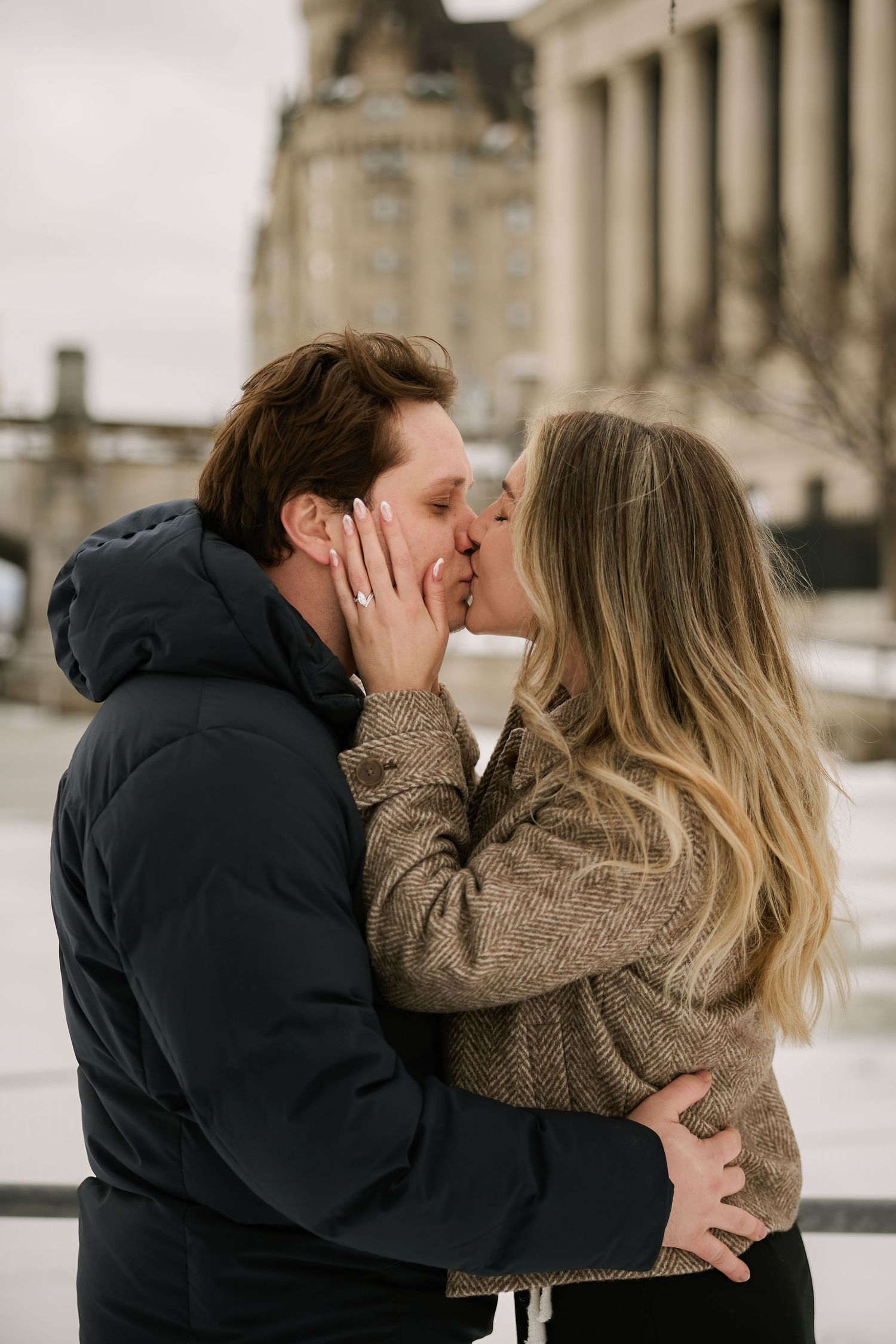 A romantic couple sharing an intimate kiss in winter against a historic building backdrop.