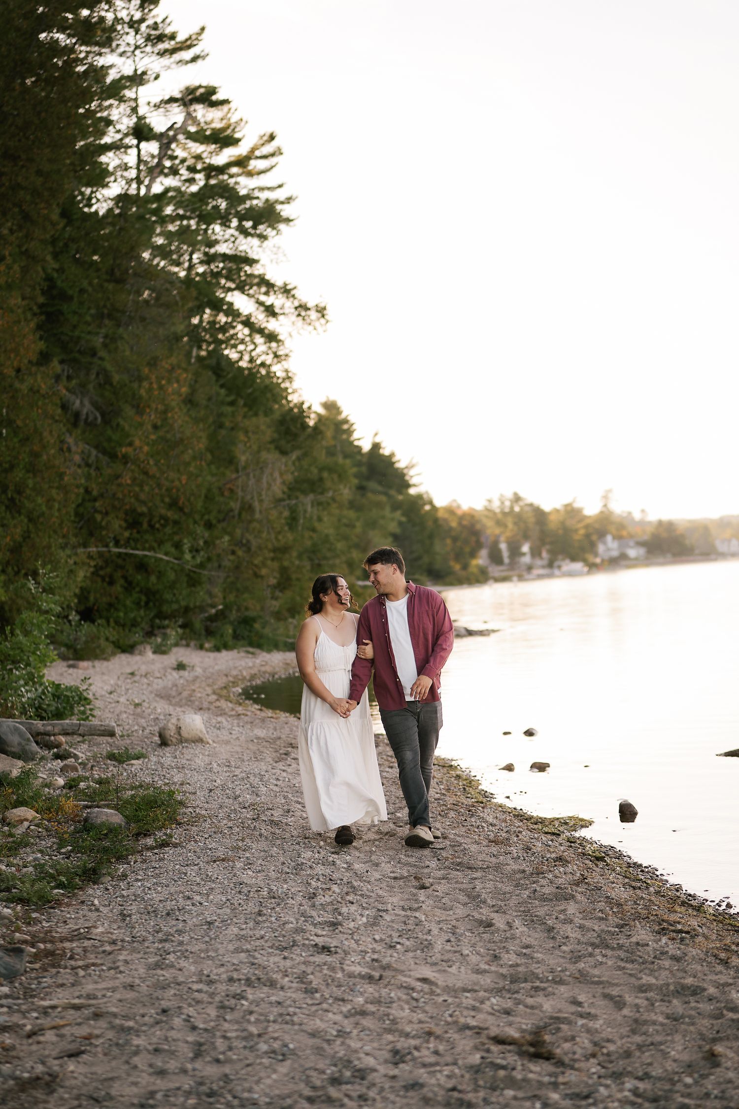 Couple walking hand in hand along a rocky beach shoreline at sunset.