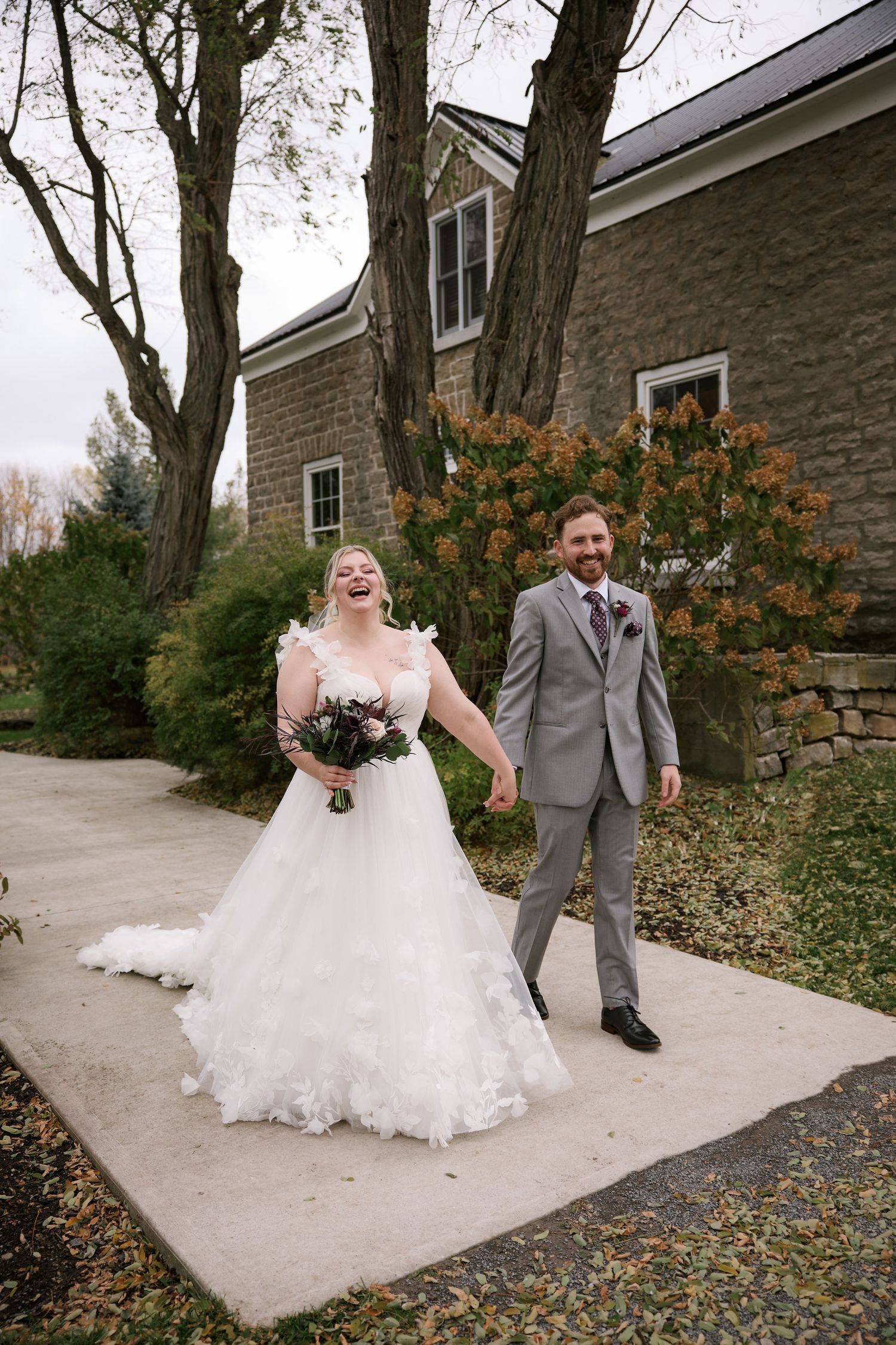 A couple laughs together on a stone pathway outside a rustic building.