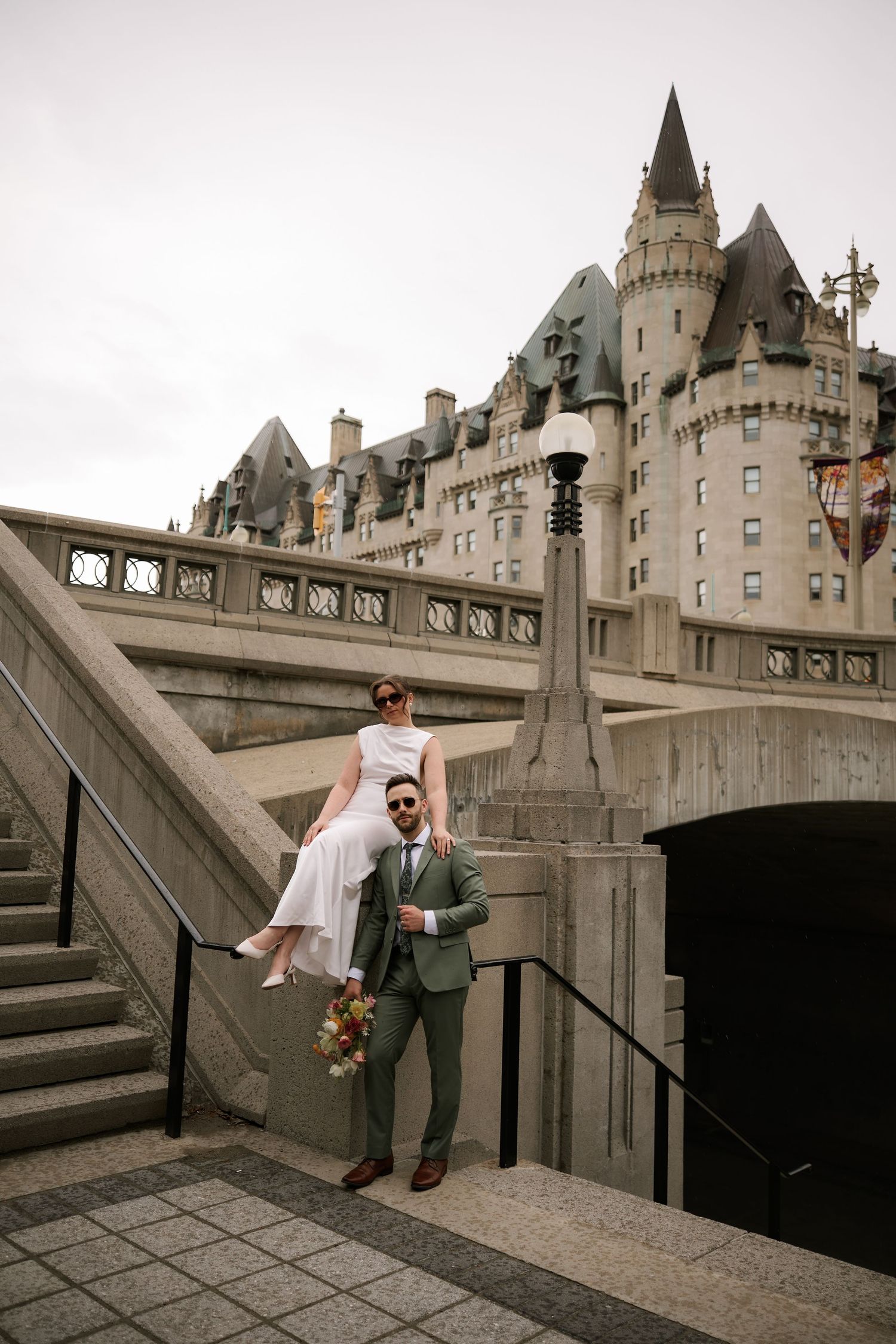 Bride sitting on groom's shoulders on stone steps with Chateau Laurier castle backdrop in Ottawa, Canada.