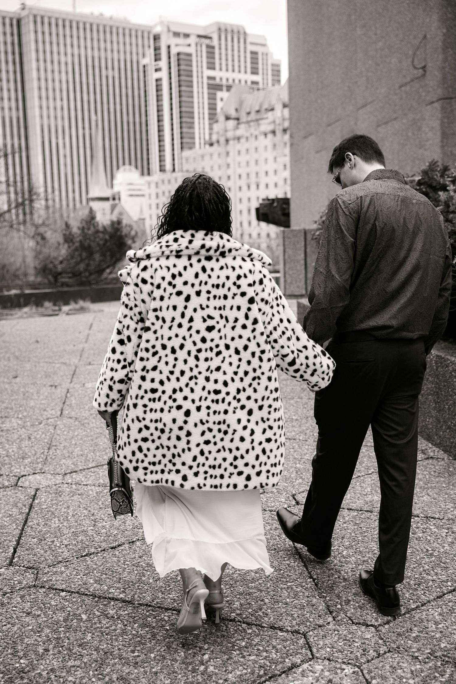 Black and white photo of a couple walking in the city, woman wearing a dalmatian print fur coat and white skirt.